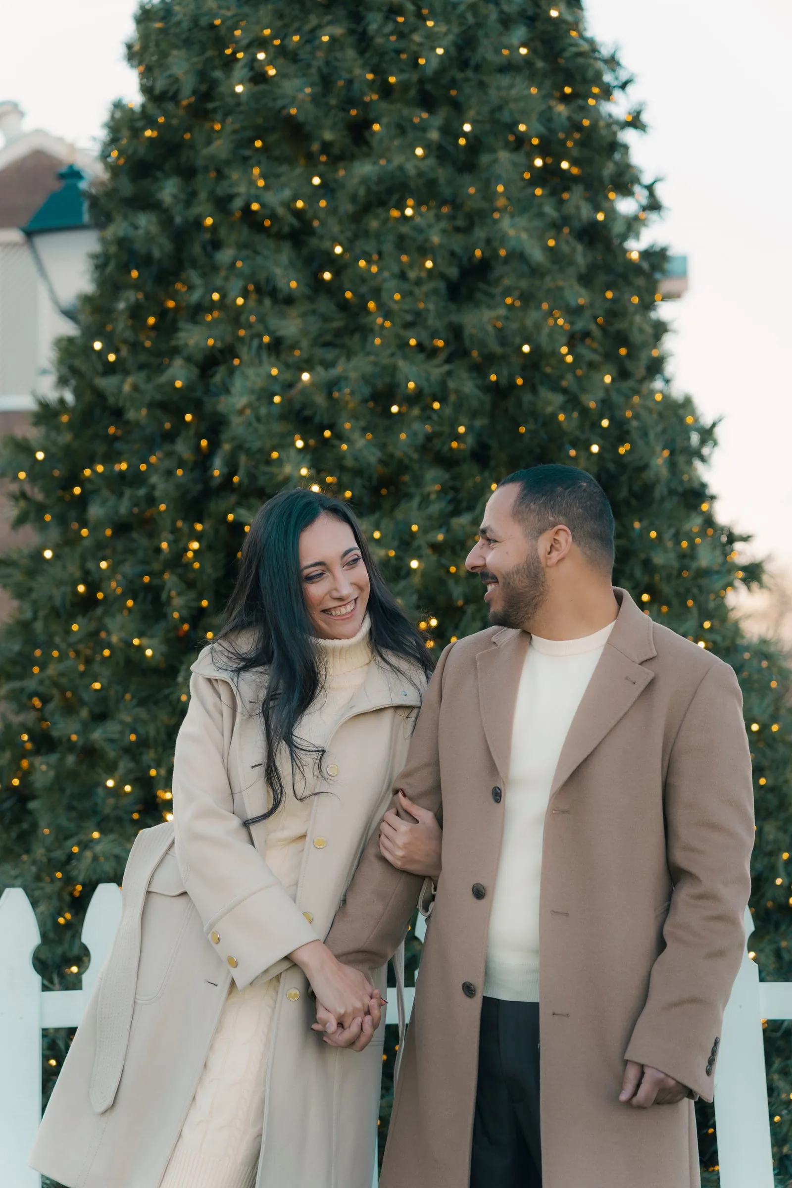 Abanoub and Merona laughing together, hands clasped, in front of the glowing Christmas tree