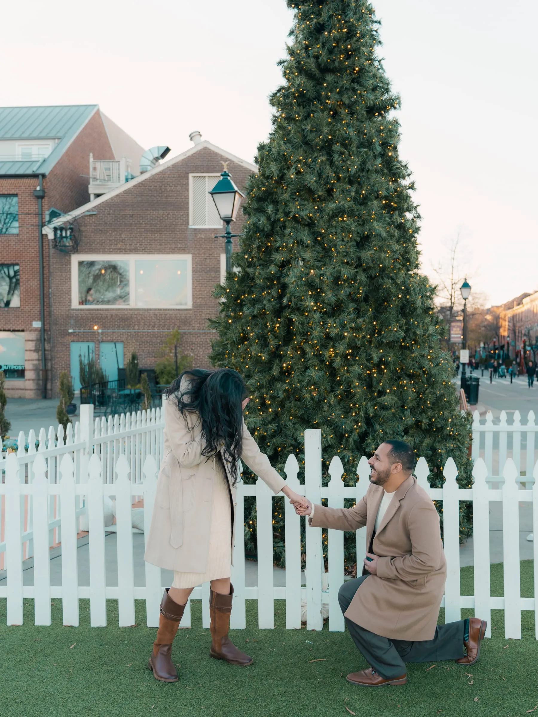 Merona reaching back for Abanoub's hand while Abanoub kneels on the lawn beneath the Christmas tree