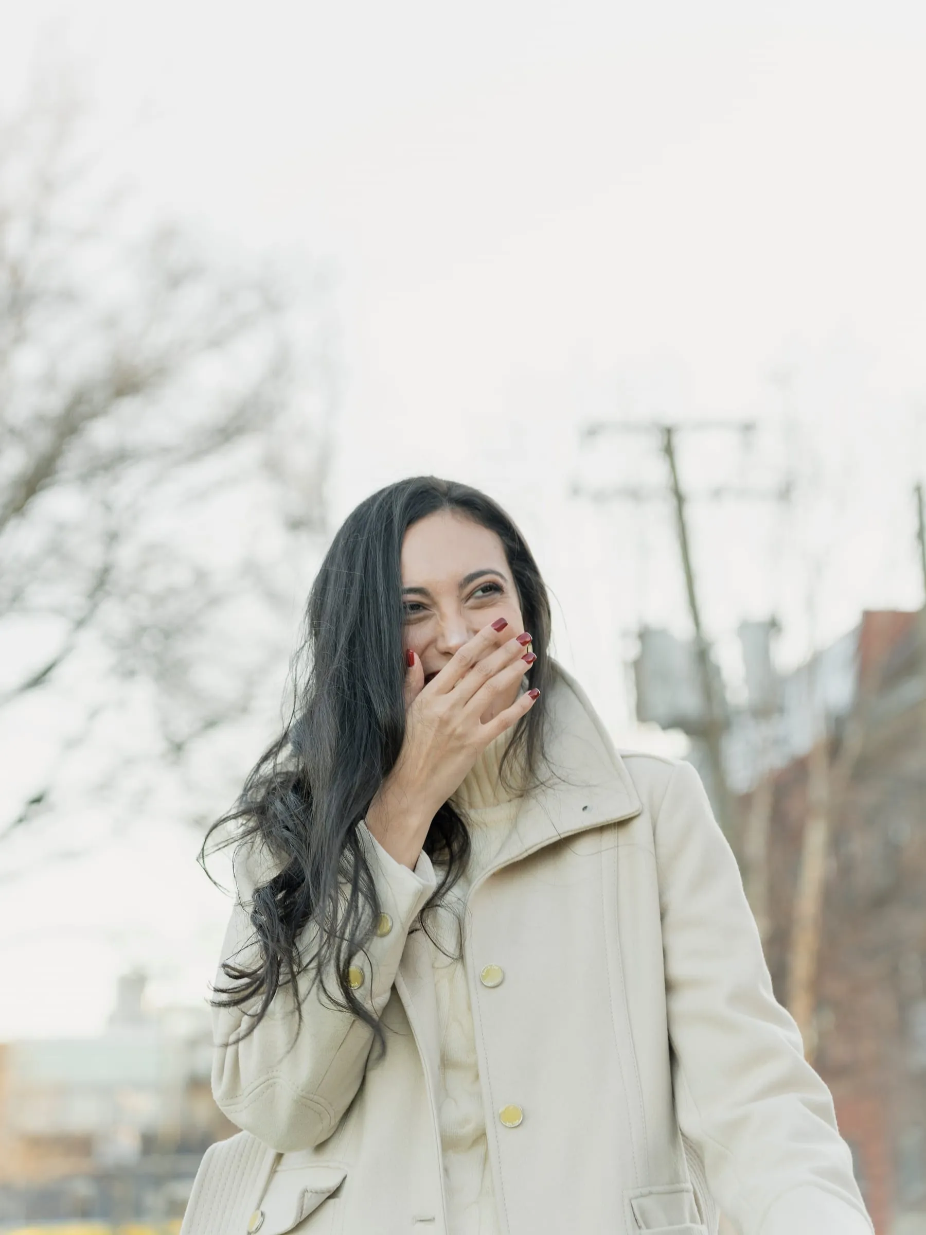 Merona laughing in surprise, one hand over mouth, in a cream winter coat