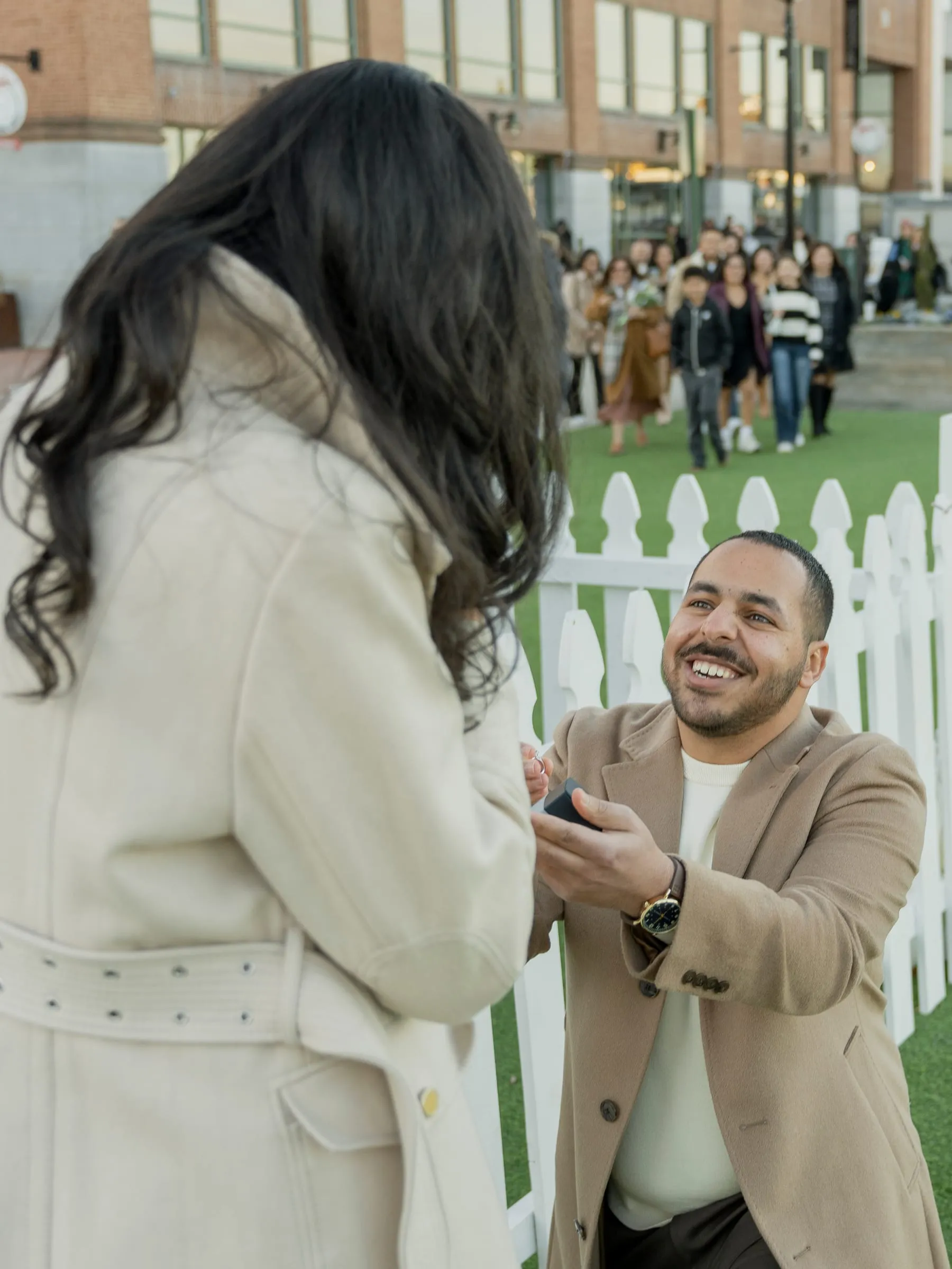 Abanoub grinning up at Merona with the ring as their friends watch from the edge of the lawn