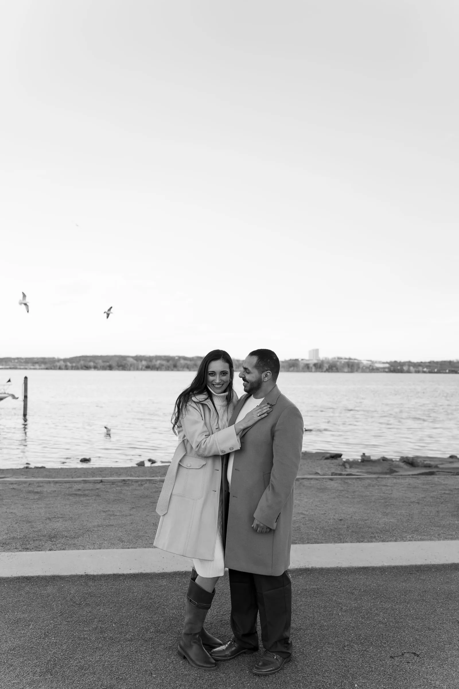 Black and white photo of Abanoub and Merona holding each other by the Potomac River, gulls overhead
