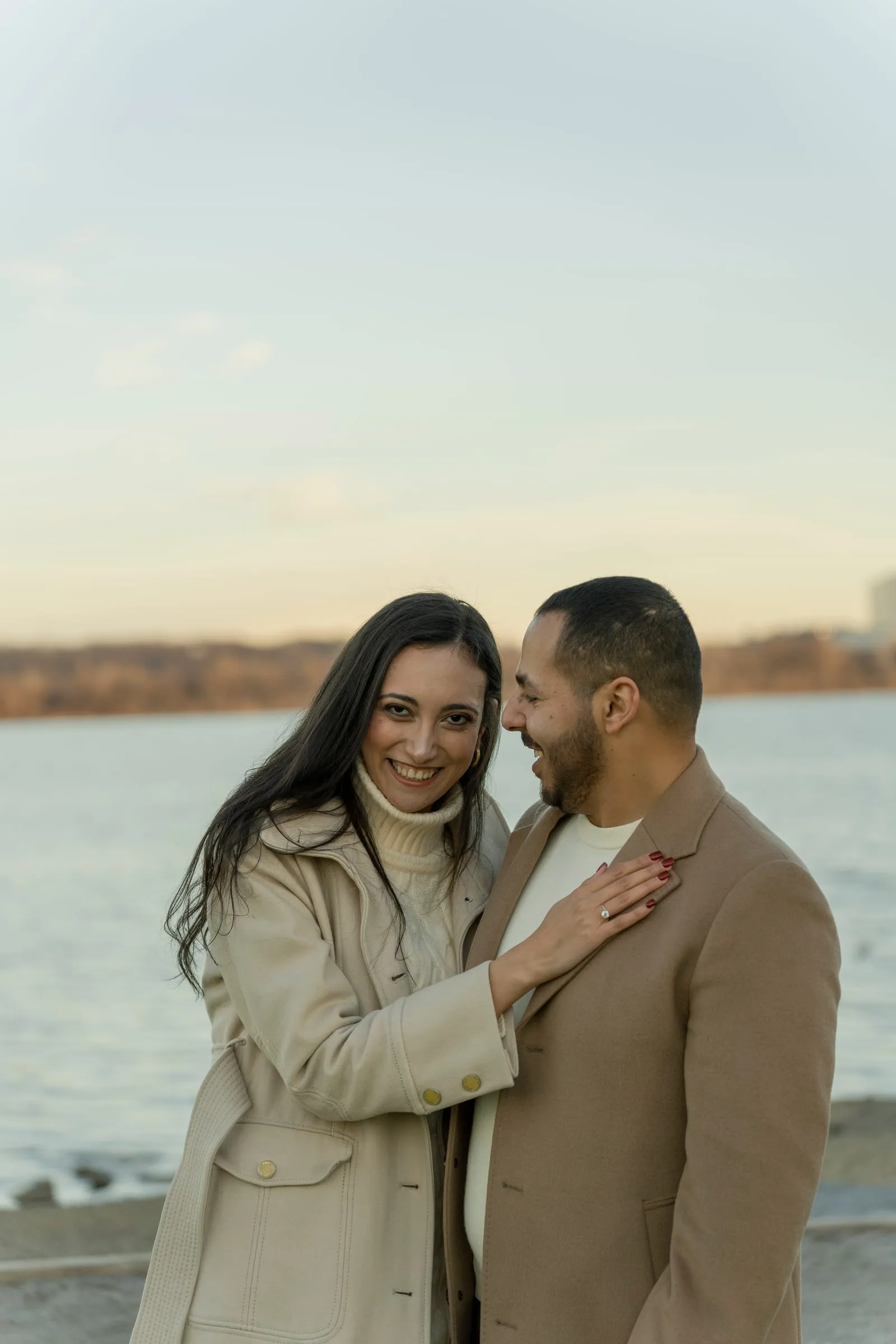 Abanoub and Merona cheek to cheek by the river, Merona's ring hand resting on Abanoub's coat