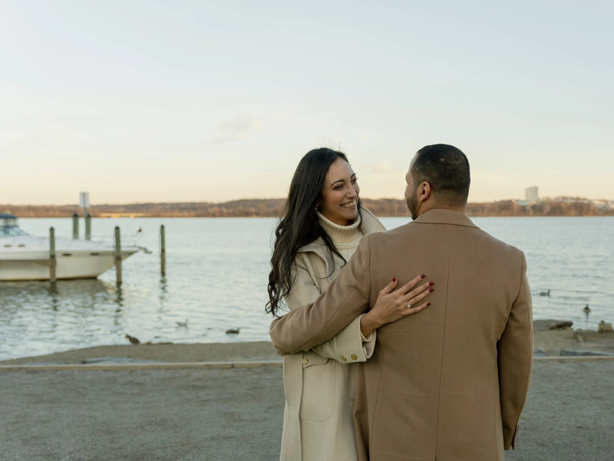 Merona smiling over Abanoub's shoulder in an embrace beside the river and a small dock