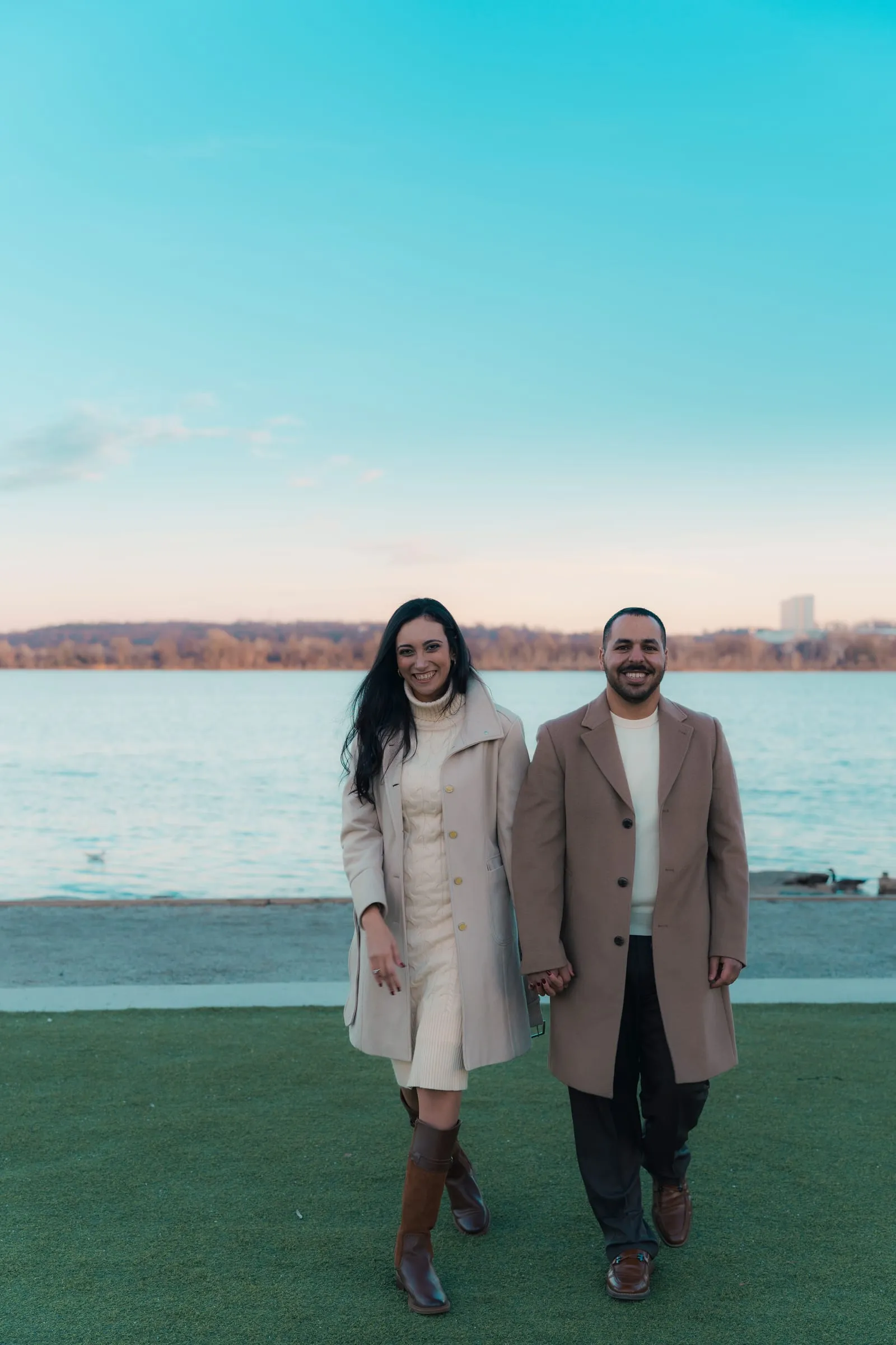 Abanoub and Merona walking hand in hand along the waterfront under a bright blue sky