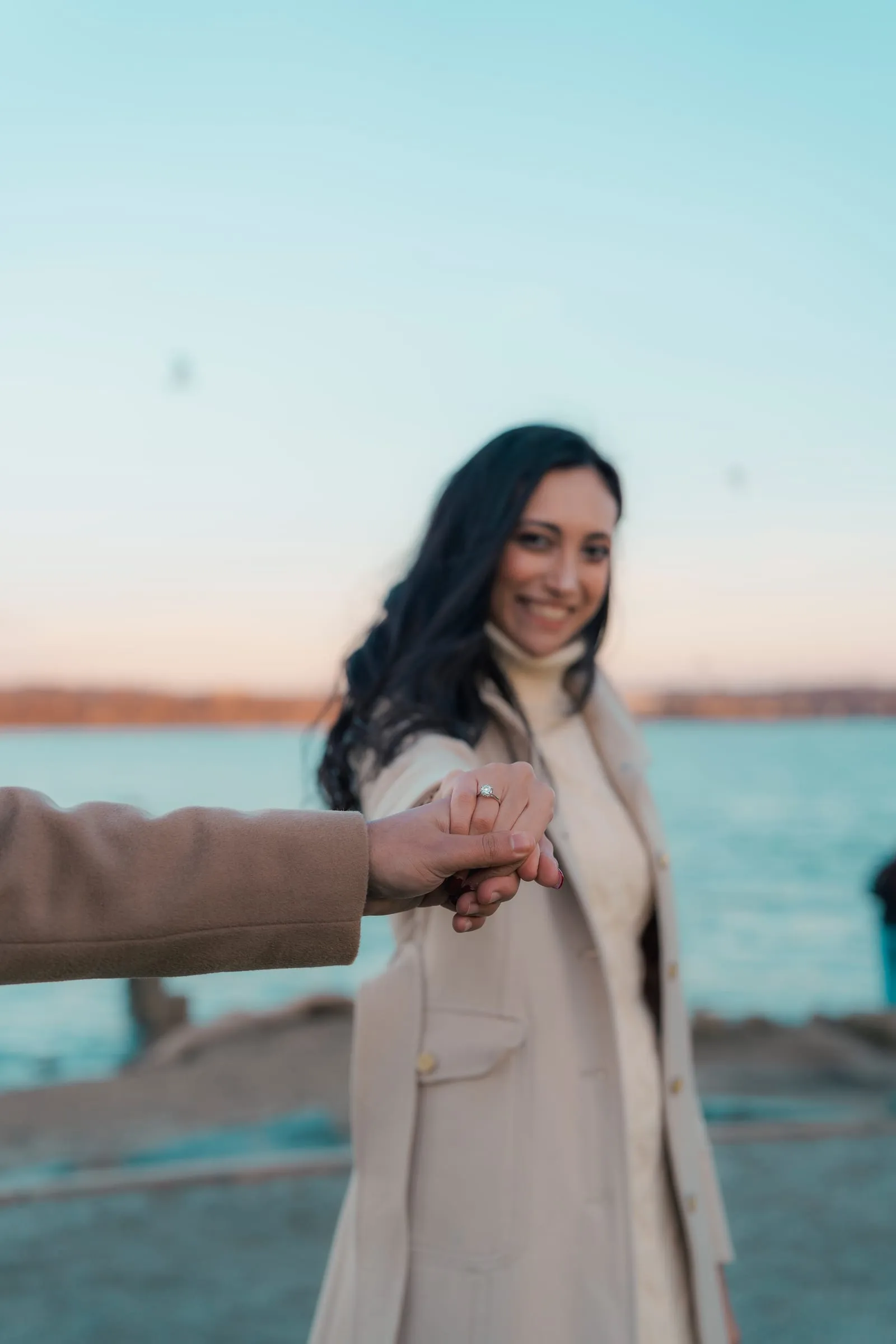 Merona looking back with a smile, holding Abanoub's hand at the water's edge