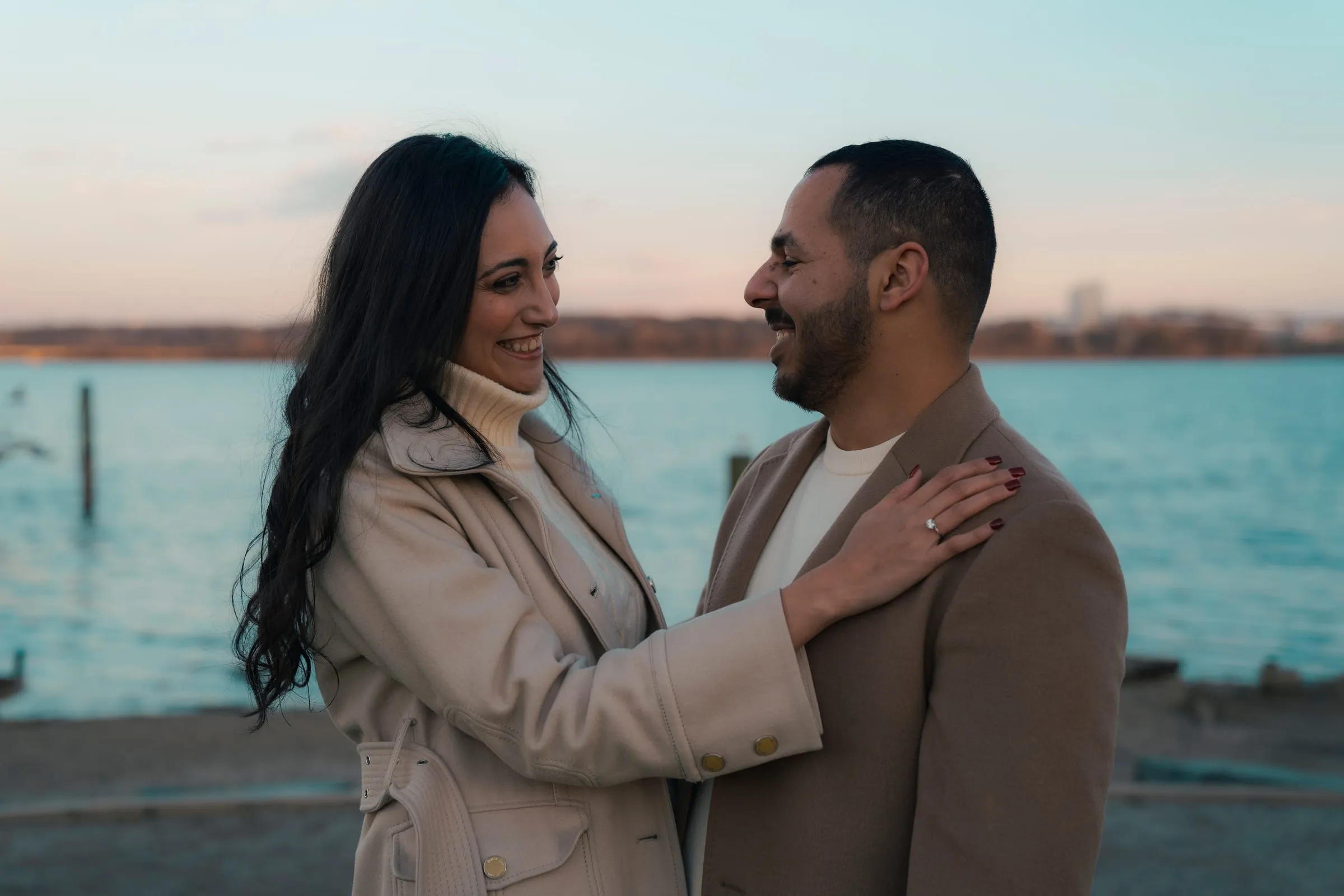 Abanoub and Merona laughing face to face by the river, Merona's ring hand on Abanoub's shoulder