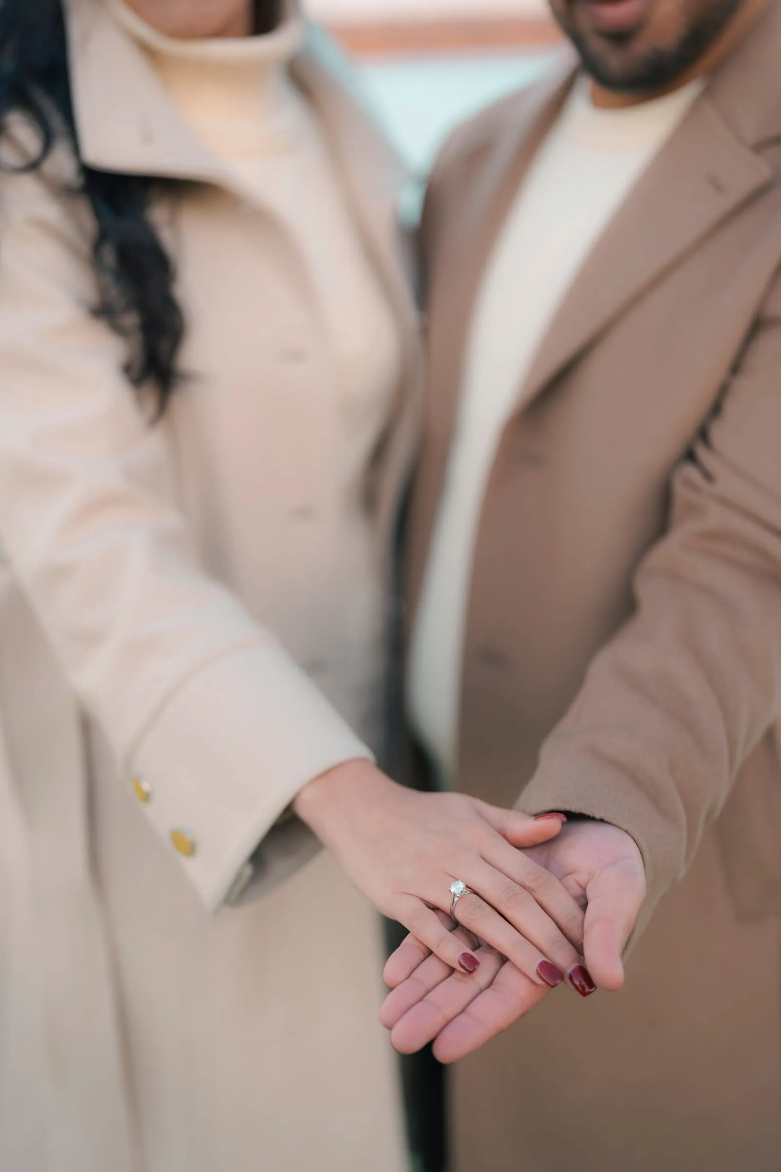 Merona's ring hand resting in Abanoub's, their coats in soft focus