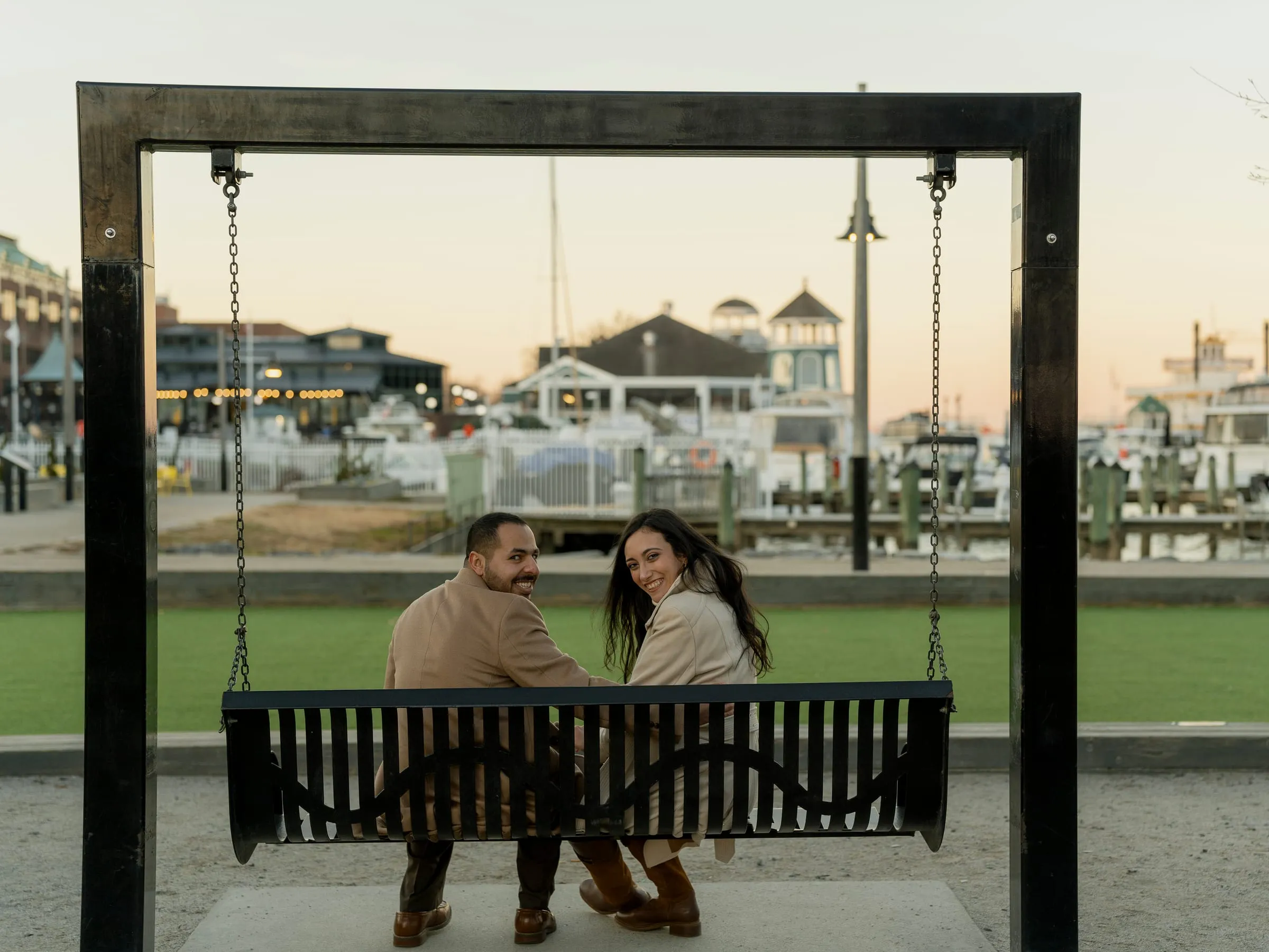 Abanoub and Merona looking back over their shoulders from a swing facing the marina