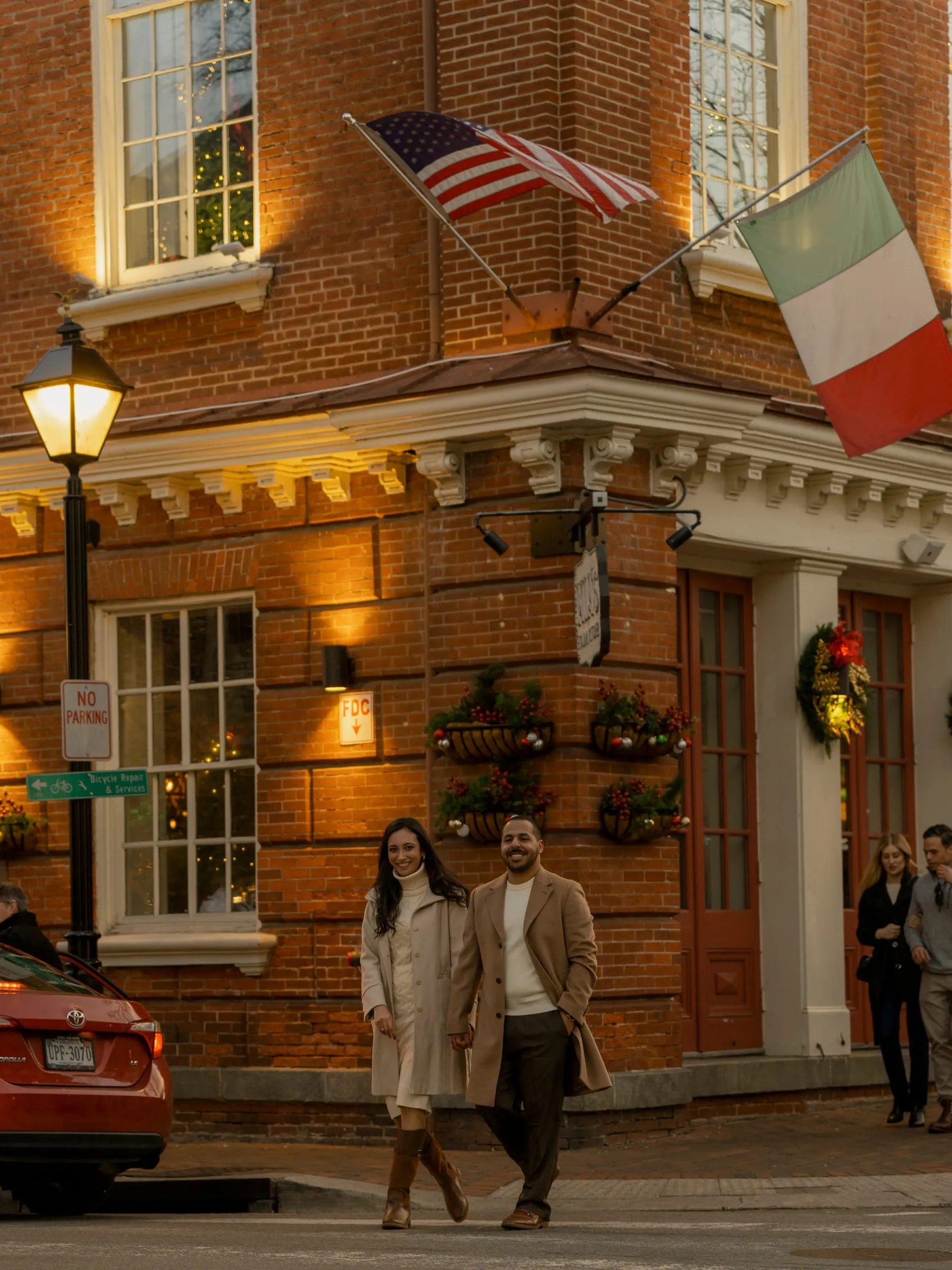 Abanoub and Merona walking past a lamplit brick building dressed for Christmas