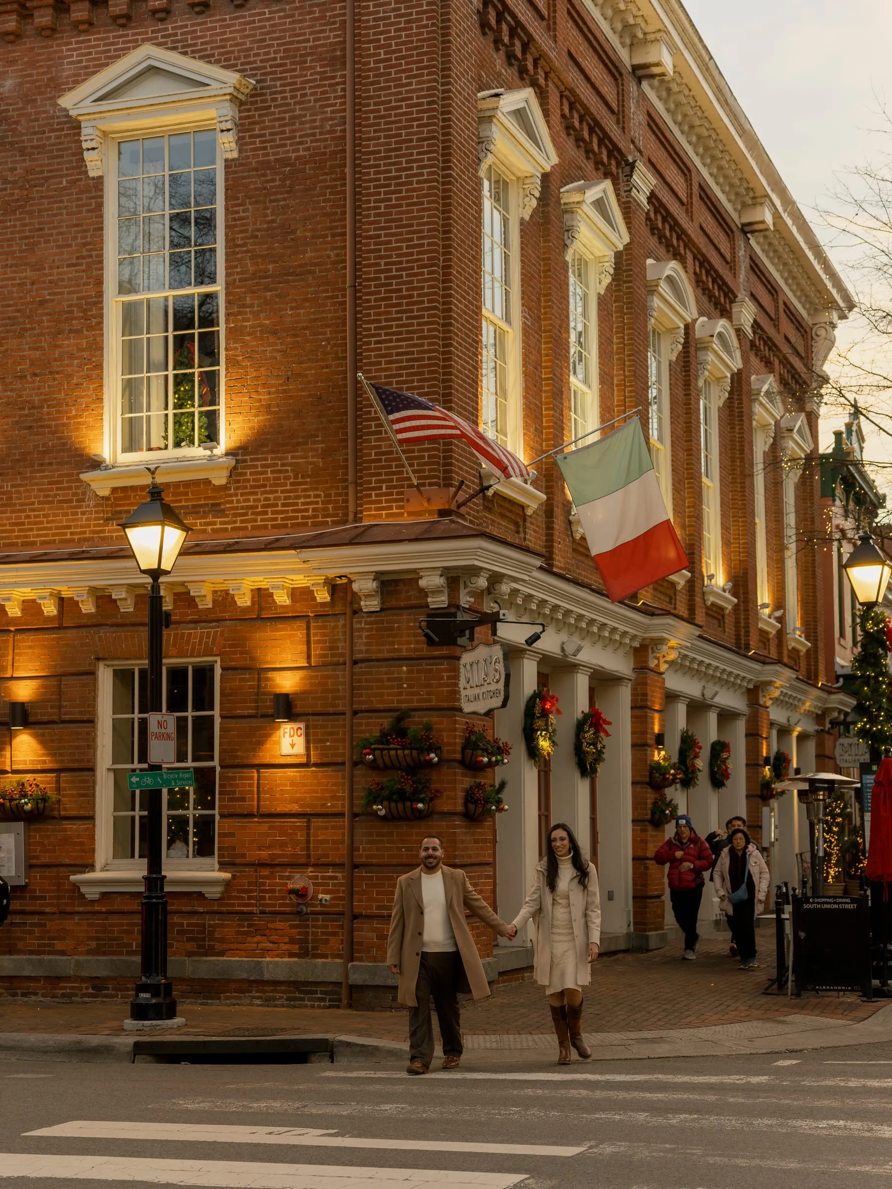 Abanoub and Merona crossing the street hand in hand beneath the flags of a historic brick corner building