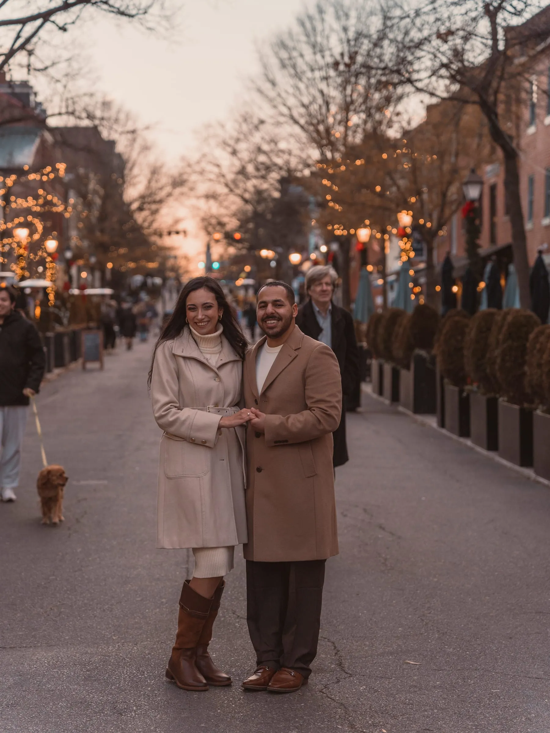 Abanoub and Merona standing hand in hand in the middle of an Old Town street strung with lights