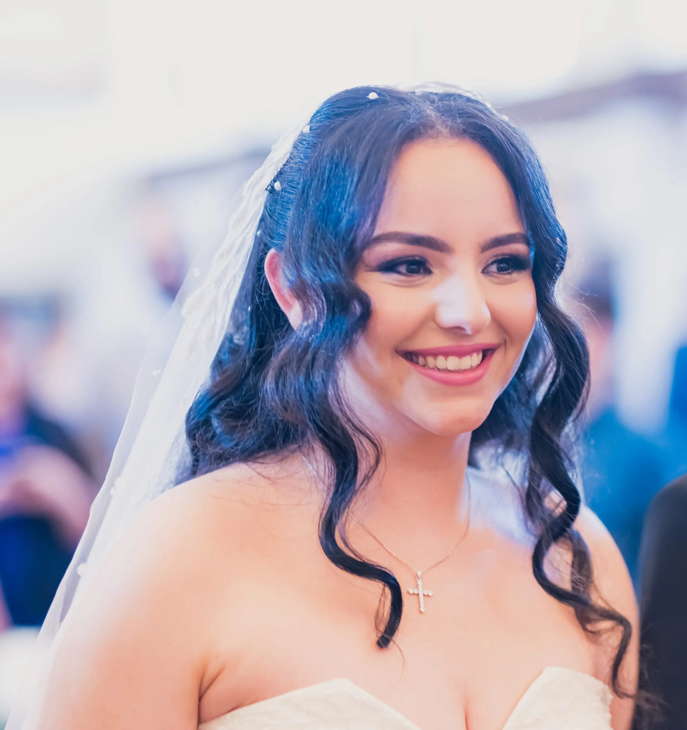 Gina smiling beneath a long veil on the way to the altar