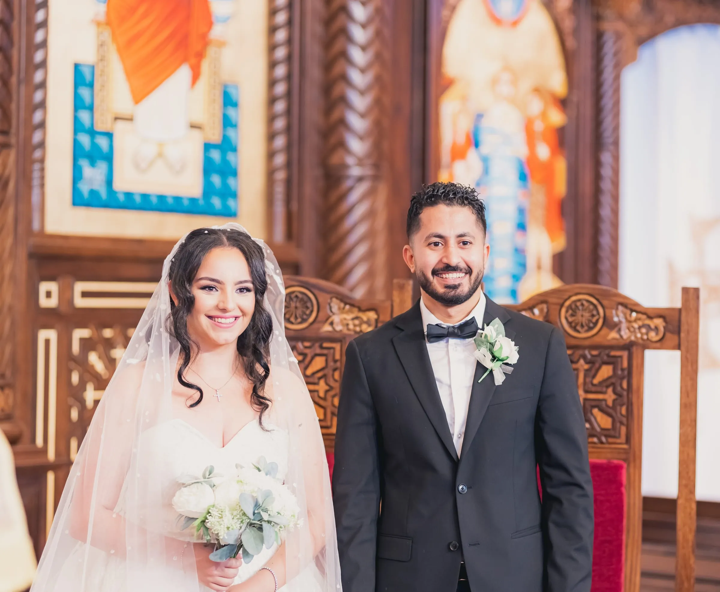 Gina and Fady smiling side by side at the altar in front of the carved wooden iconostasis