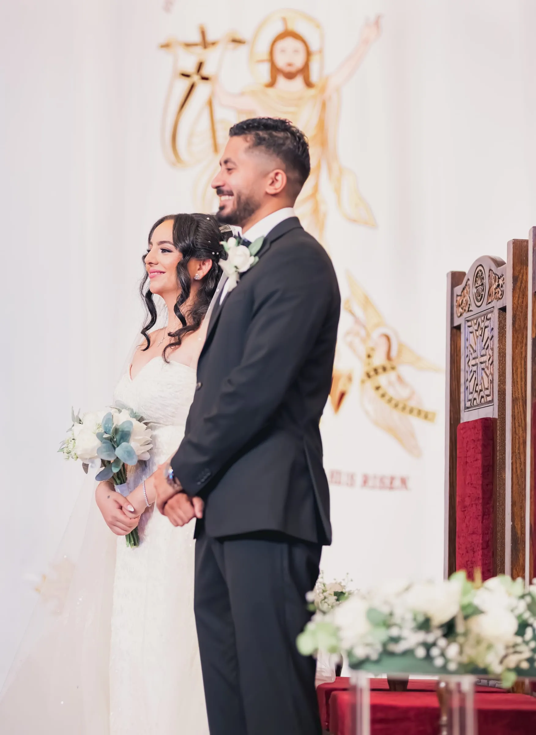 Fady smiling at Gina in front of the embroidered Christ is Risen backdrop
