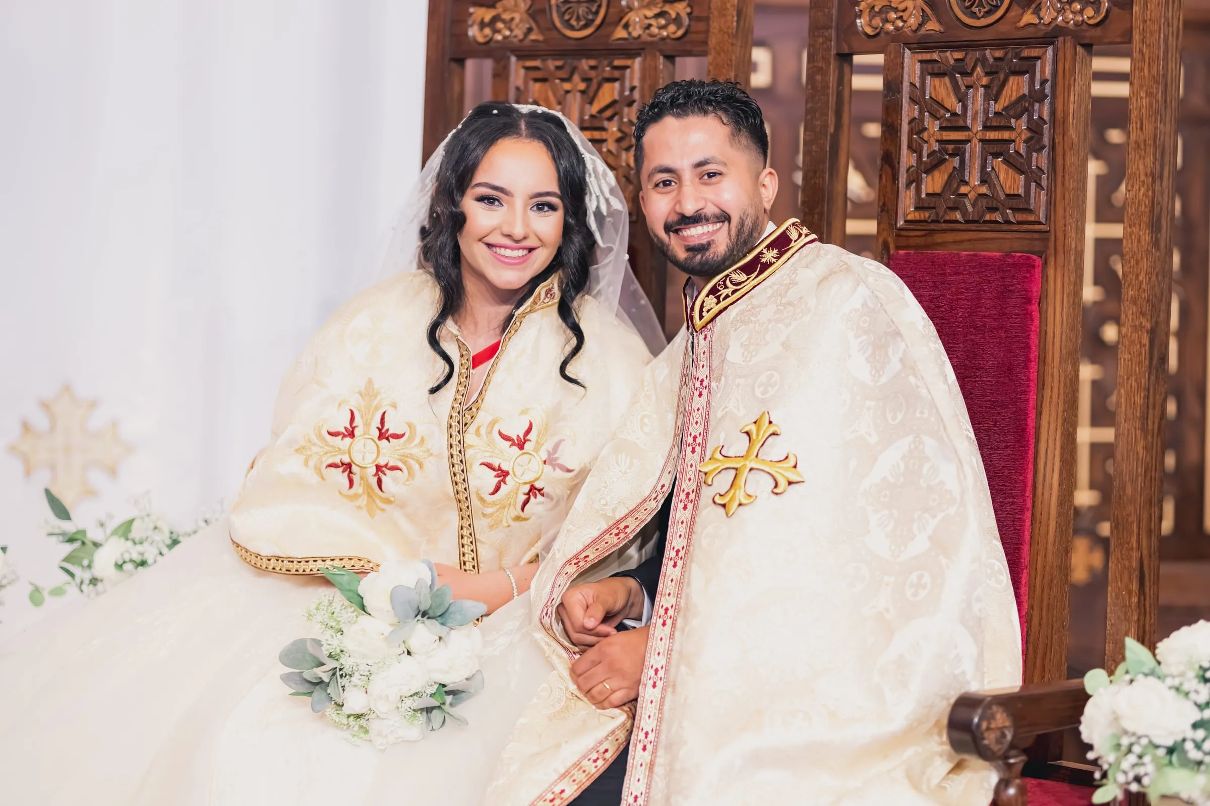 Gina and Fady seated side by side in their ceremonial robes, smiling at the camera