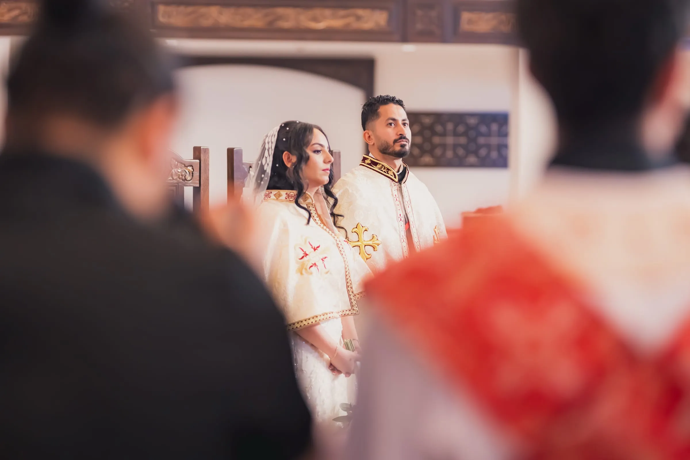 Gina and Fady in their robes, seen past the clergy during the crowning ceremony