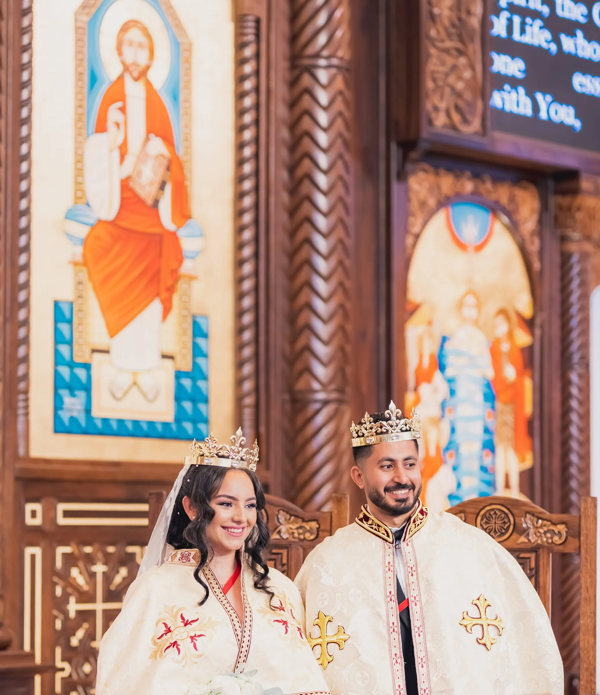 Gina and Fady crowned and seated on the wedding thrones beneath painted icons
