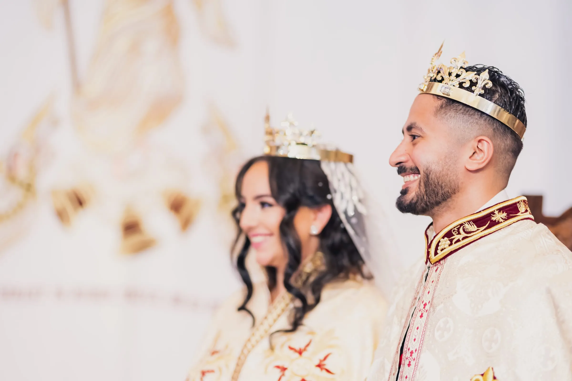 Fady smiling at Gina, both wearing gold crowns, during the crowning rite