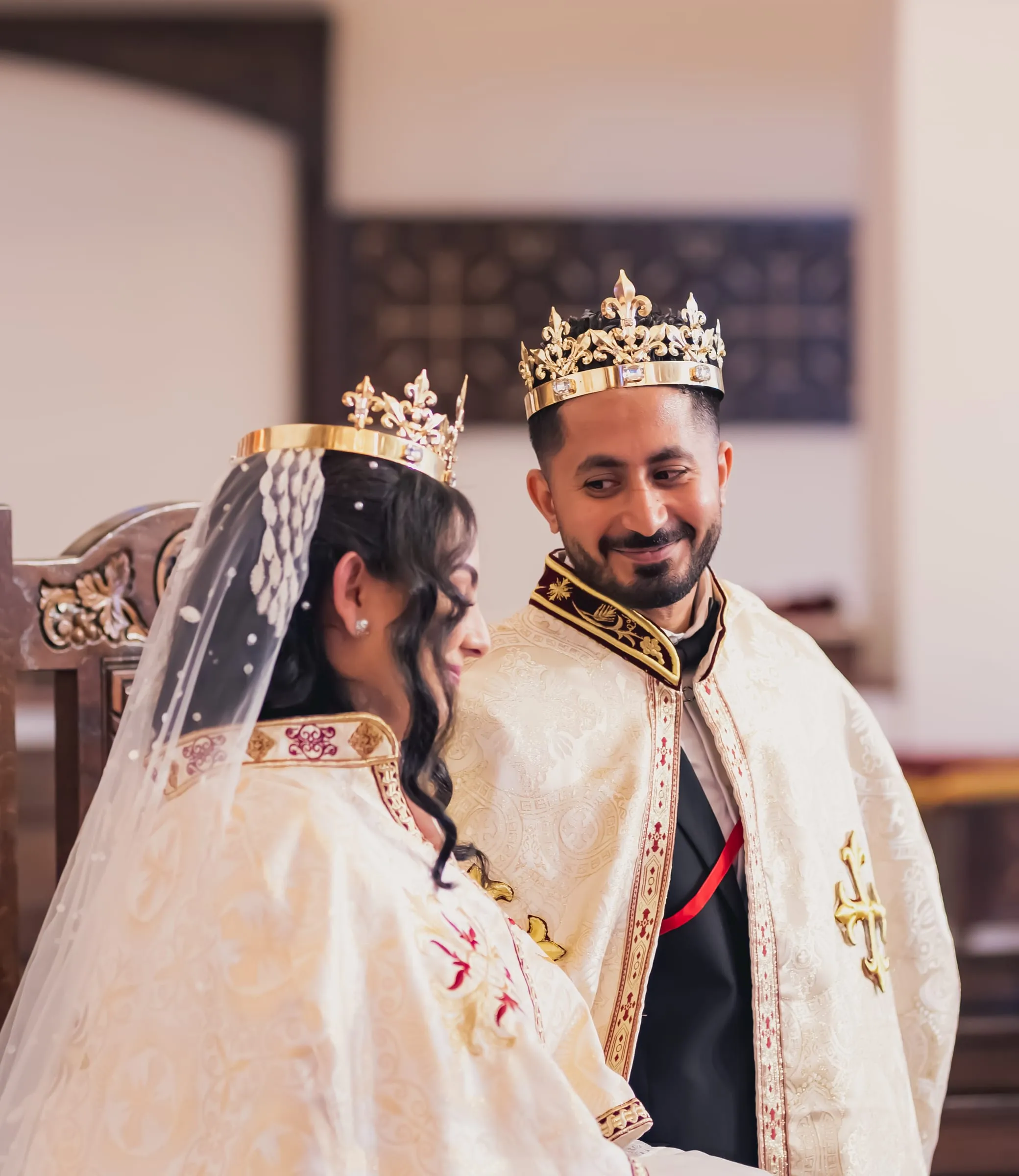 Gina and Fady smiling on the thrones in their crowns and robes, Gina's veil lit from behind