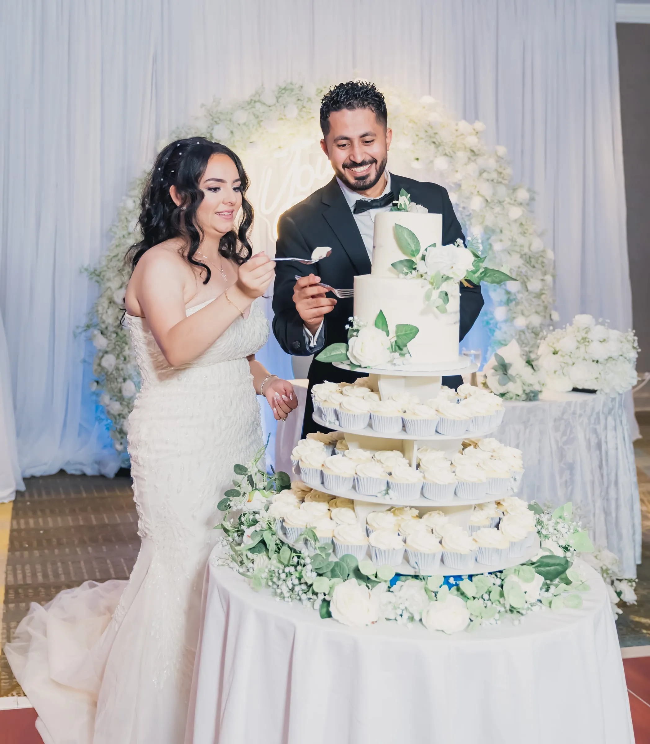 Gina and Fady feeding each other cake beside the cupcake tower