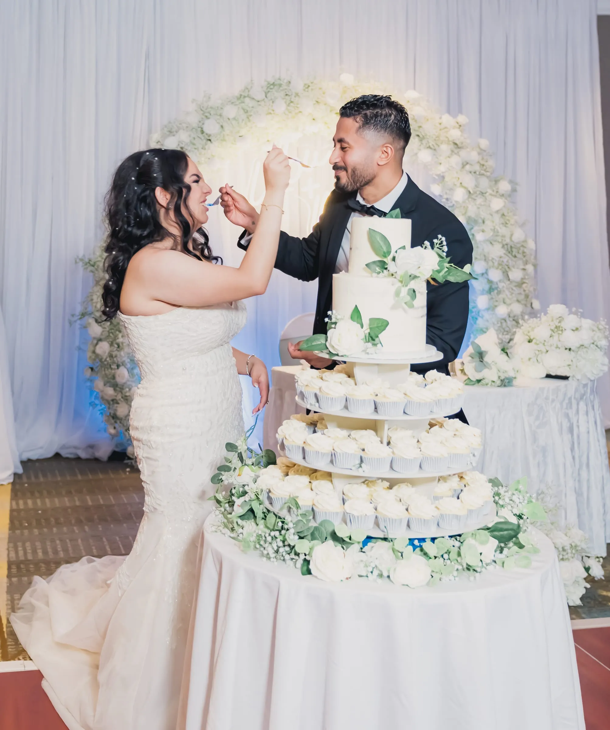Gina feeding Fady a bite of wedding cake in front of the floral arch