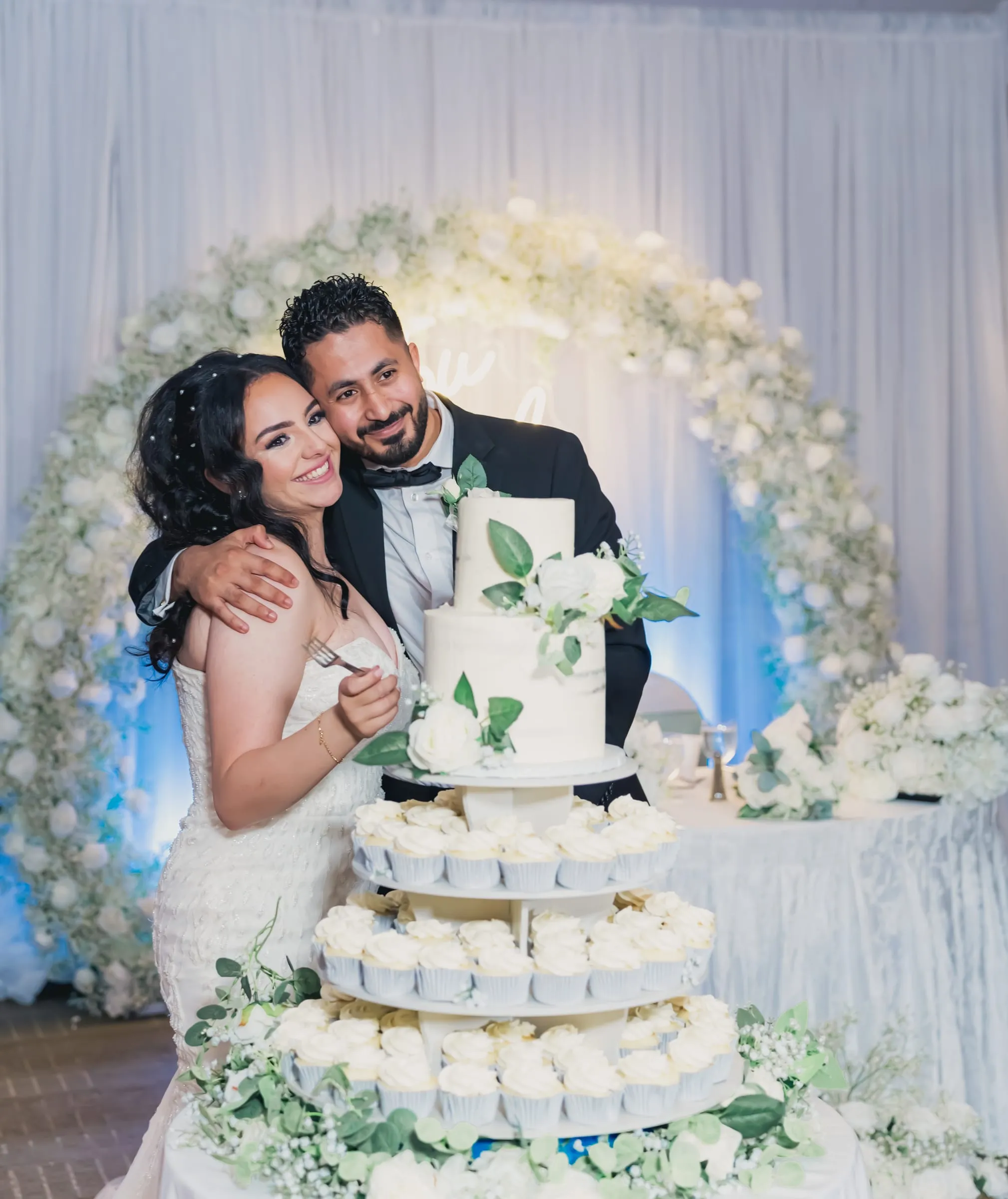 Fady hugging Gina close as they smile behind the wedding cake