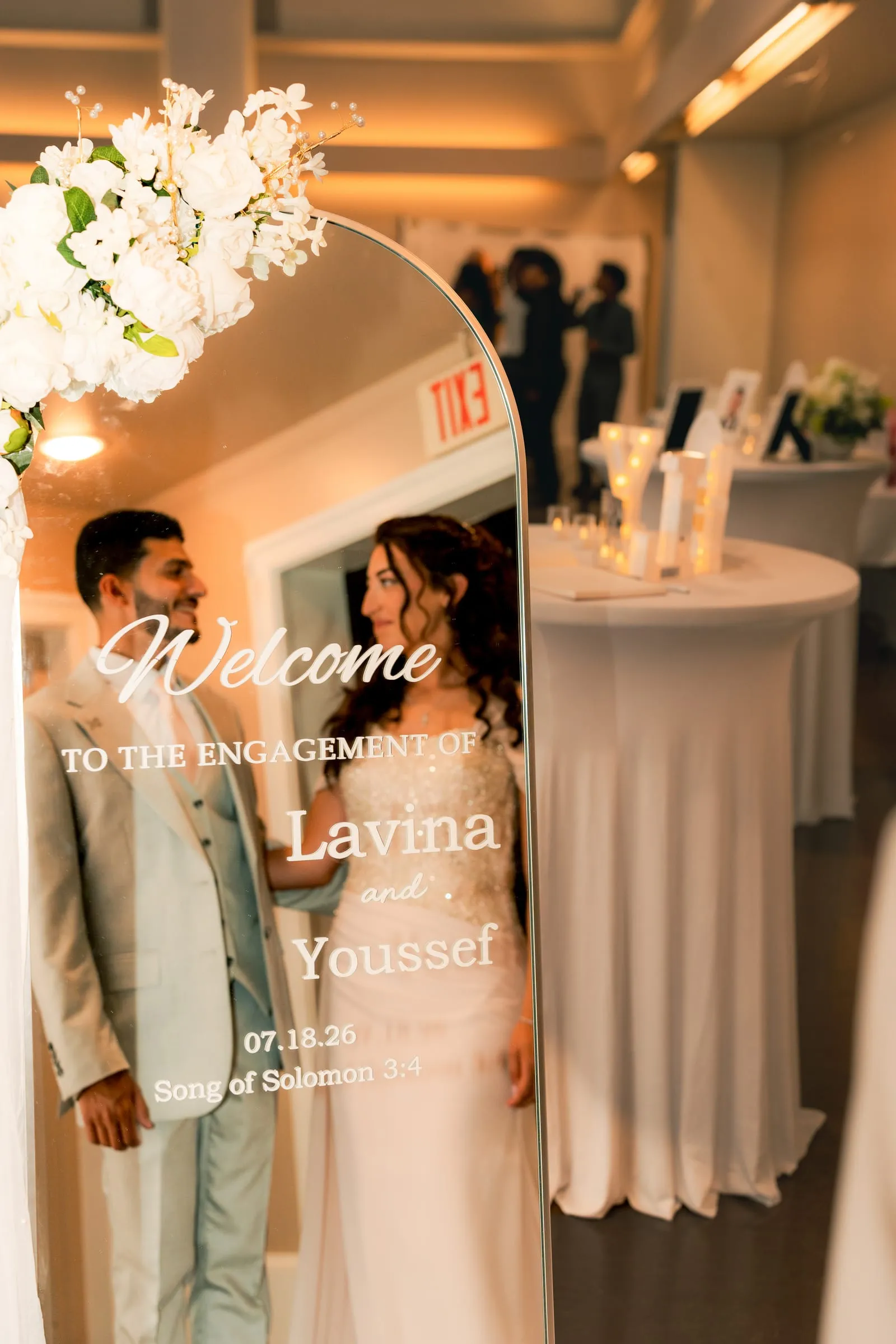 Lavina and Youssef gazing at each other through the mirrored welcome sign at their engagement celebration