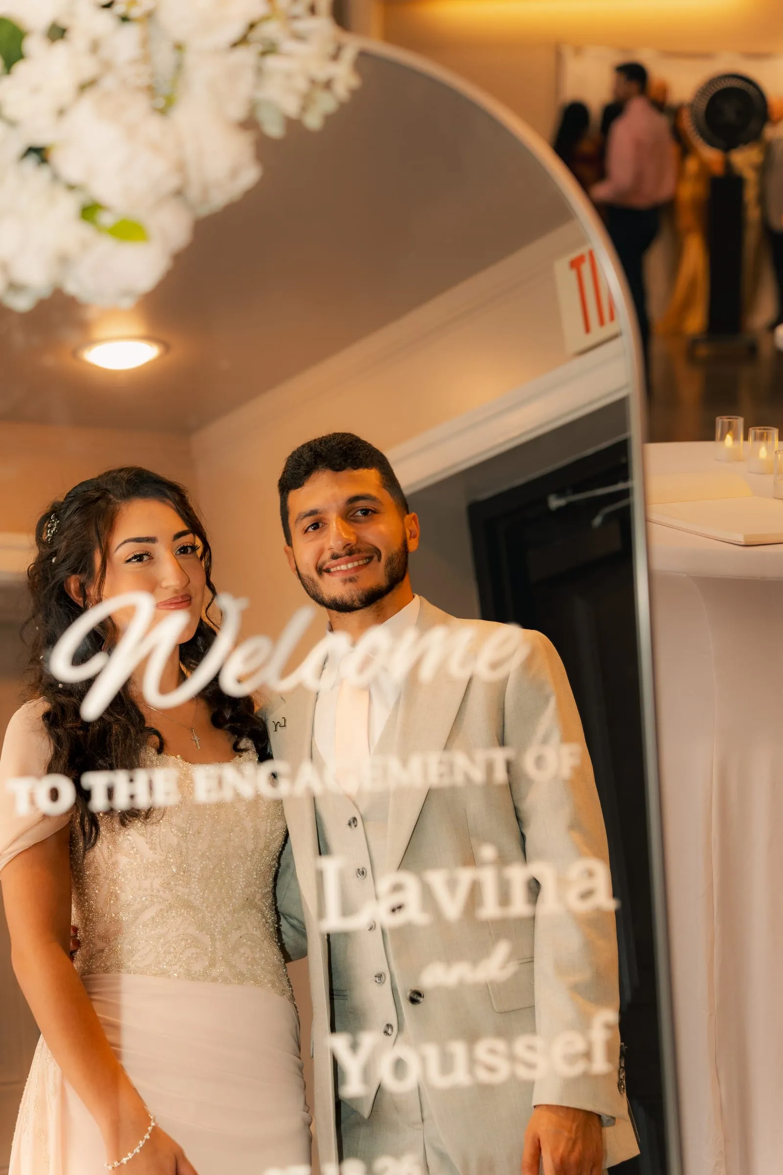 Close-up of Lavina and Youssef smiling together behind the engagement welcome sign