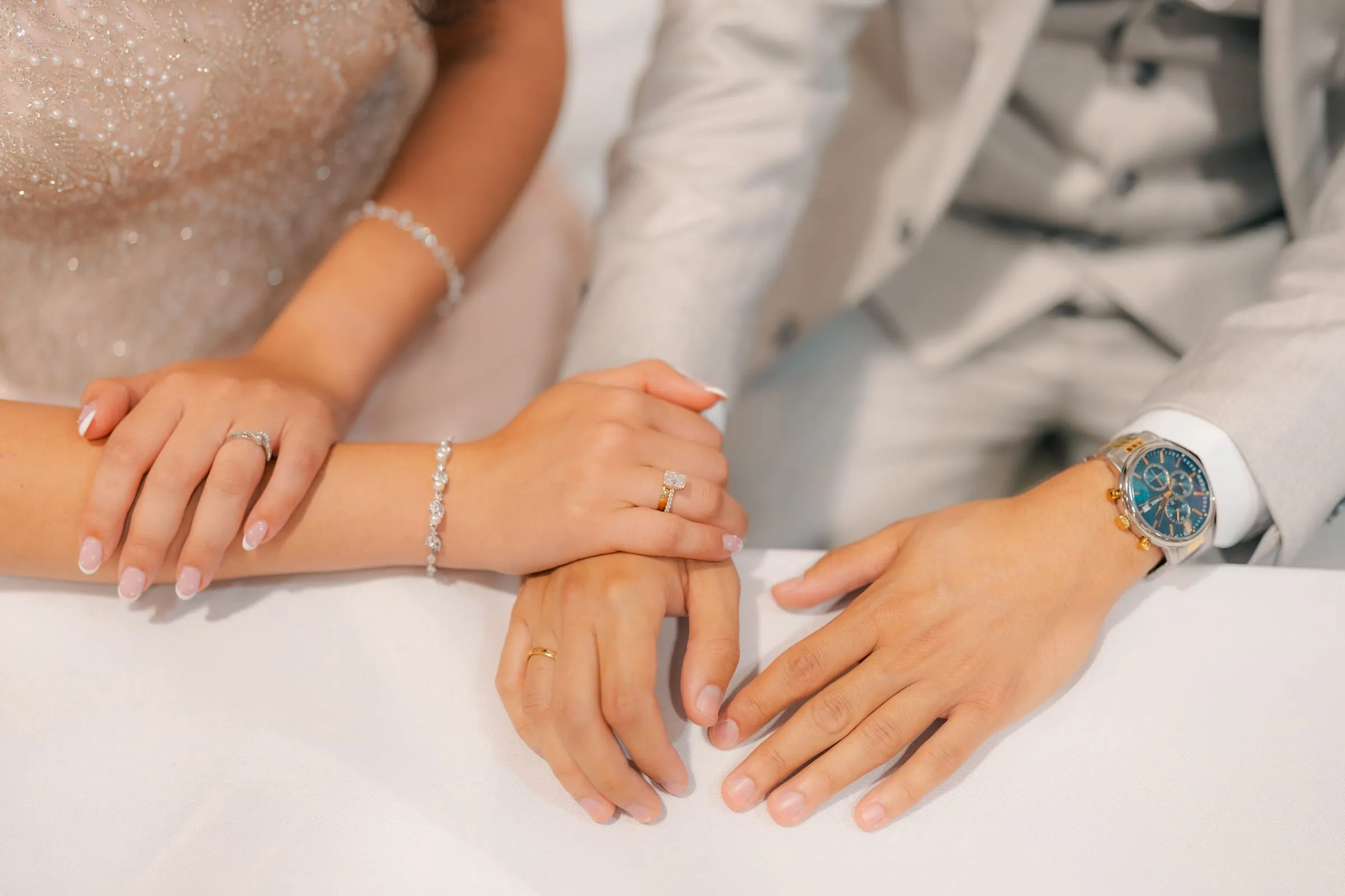 Detail of Lavina and Youssef's clasped hands showing her engagement ring and his wristwatch