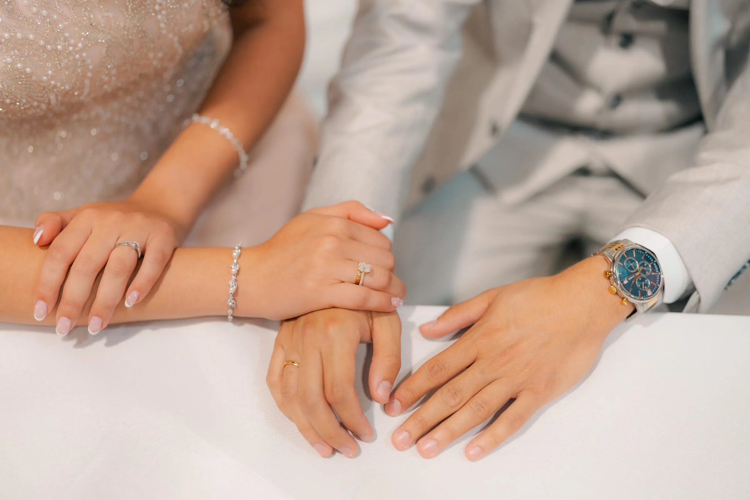 Close-up of the couple's intertwined hands and jewelry at their engagement celebration