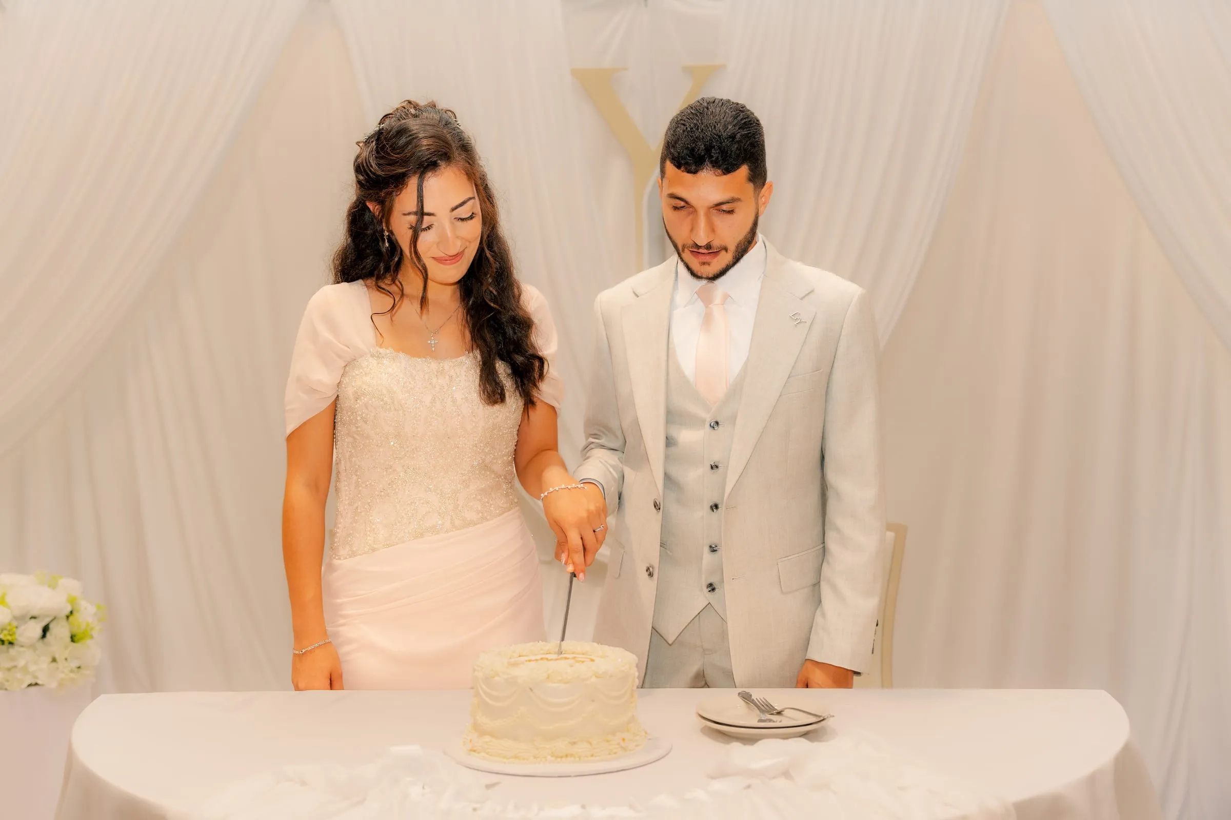 Lavina and Youssef looking down as they cut their engagement cake together