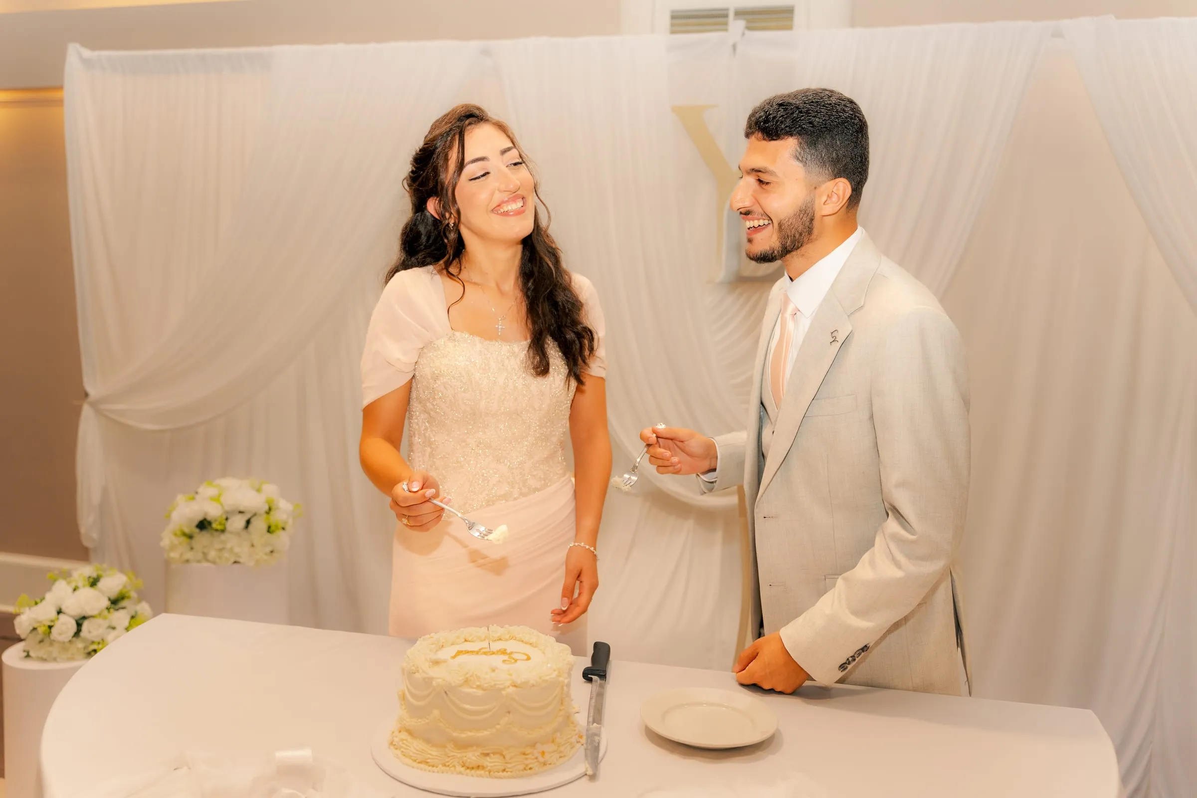 Lavina and Youssef laughing with forks in hand, about to feed each other cake