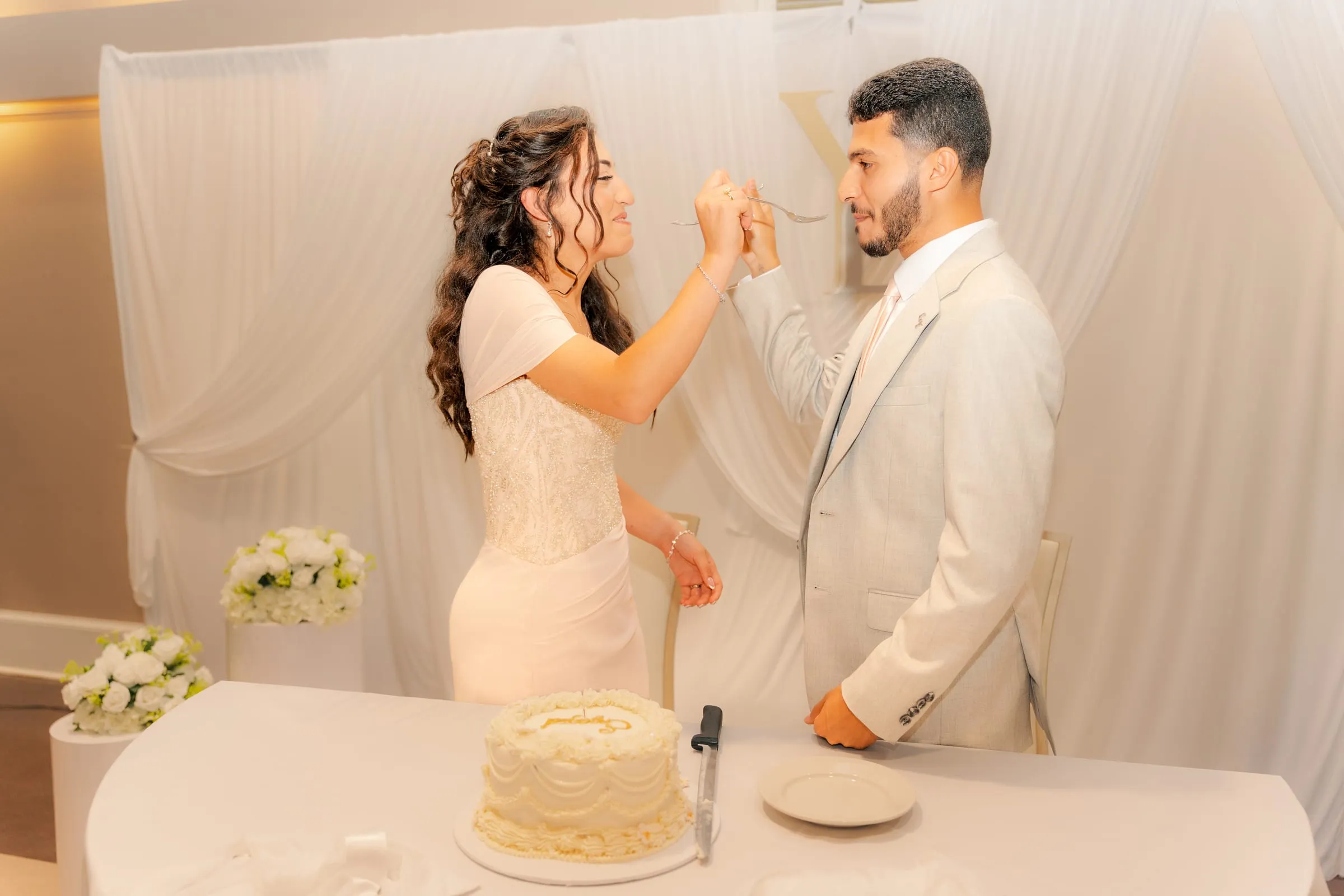 Lavina and Youssef holding forks up to feed each other cake, smiling