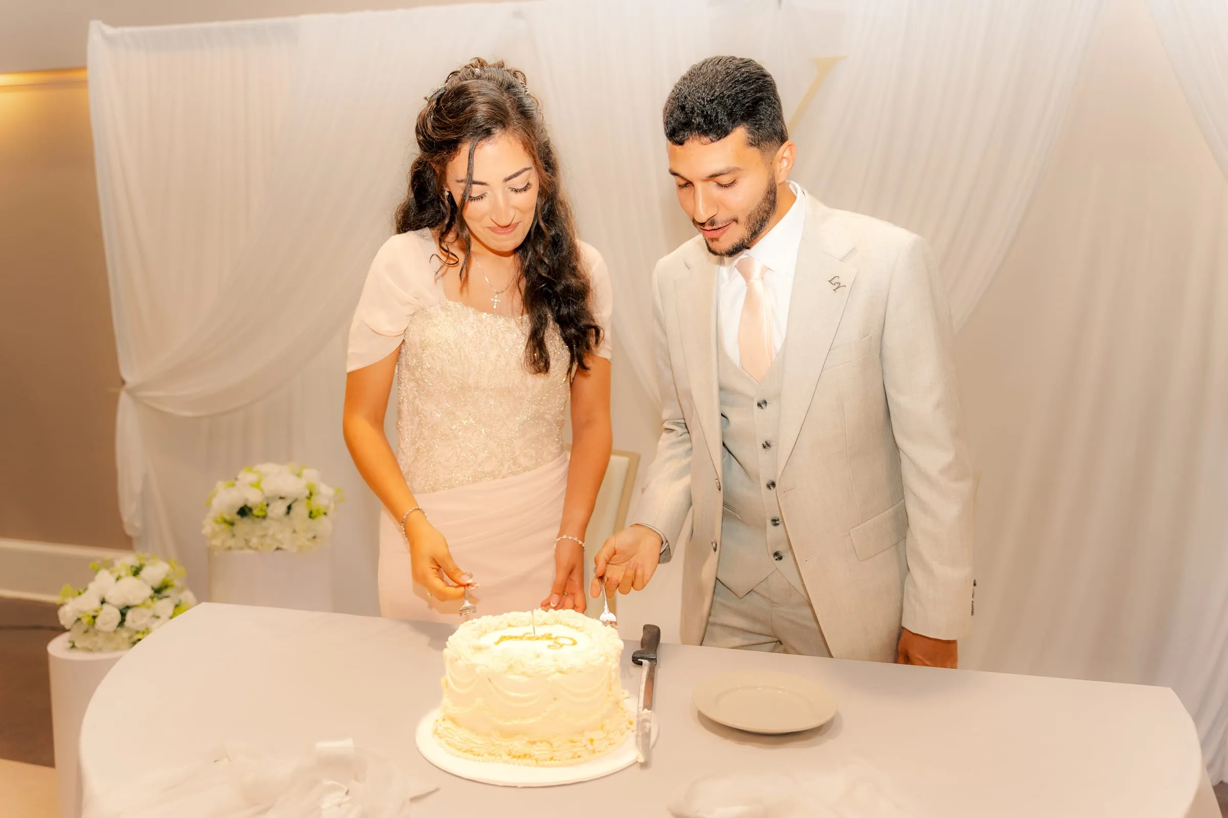Lavina and Youssef smiling together while cutting their engagement cake