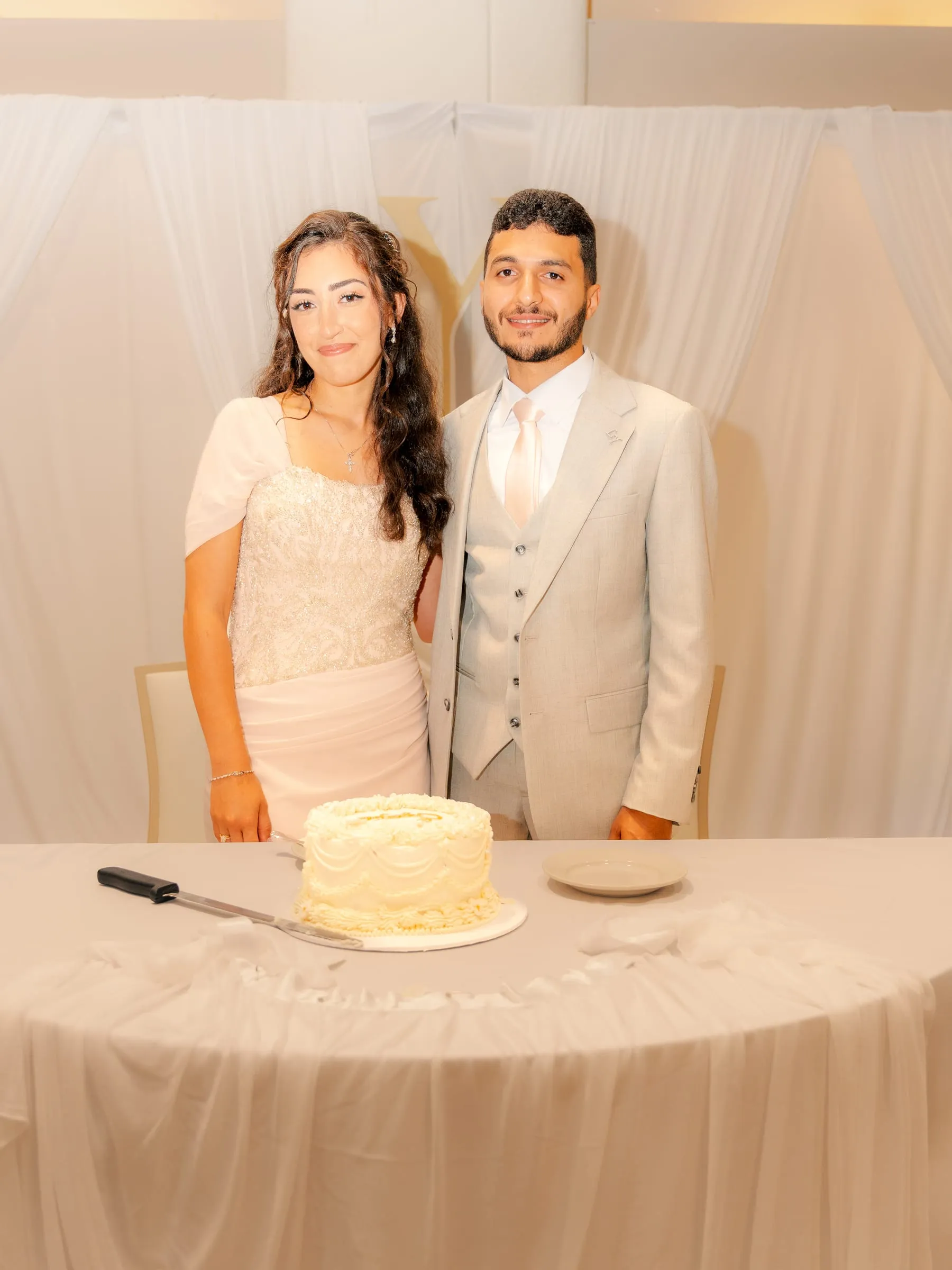 Lavina and Youssef standing behind the cake table smiling at the camera