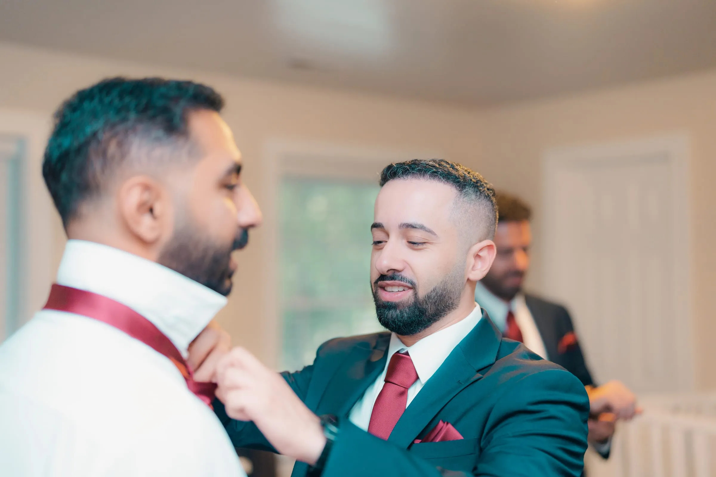 A groomsman adjusting another man's red tie while getting ready for Mariam and Mina's wedding