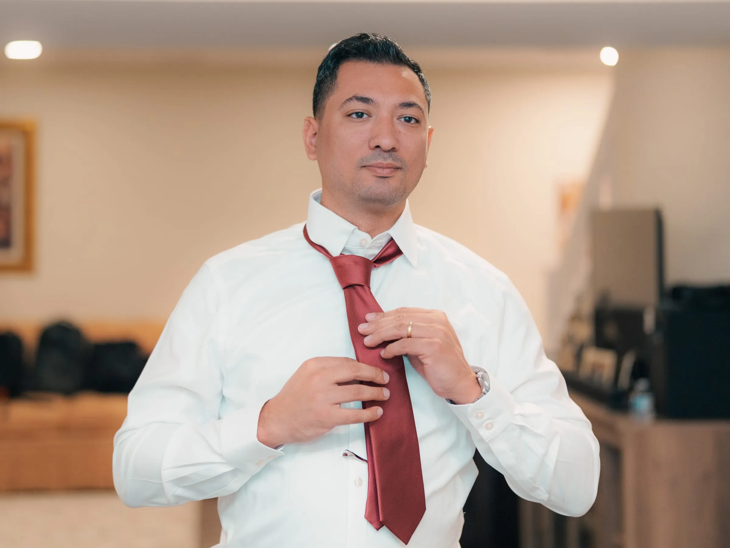 A groomsman tying his red tie while getting ready for the wedding