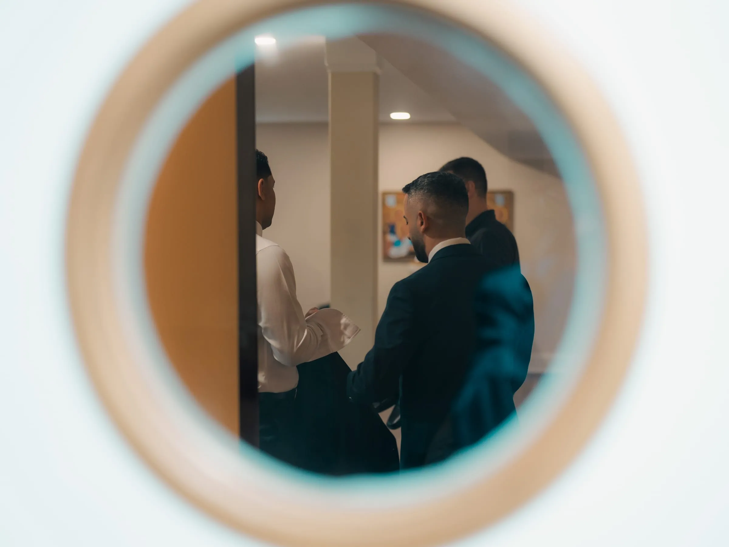 Groomsmen reflected in a round mirror while getting ready for the wedding