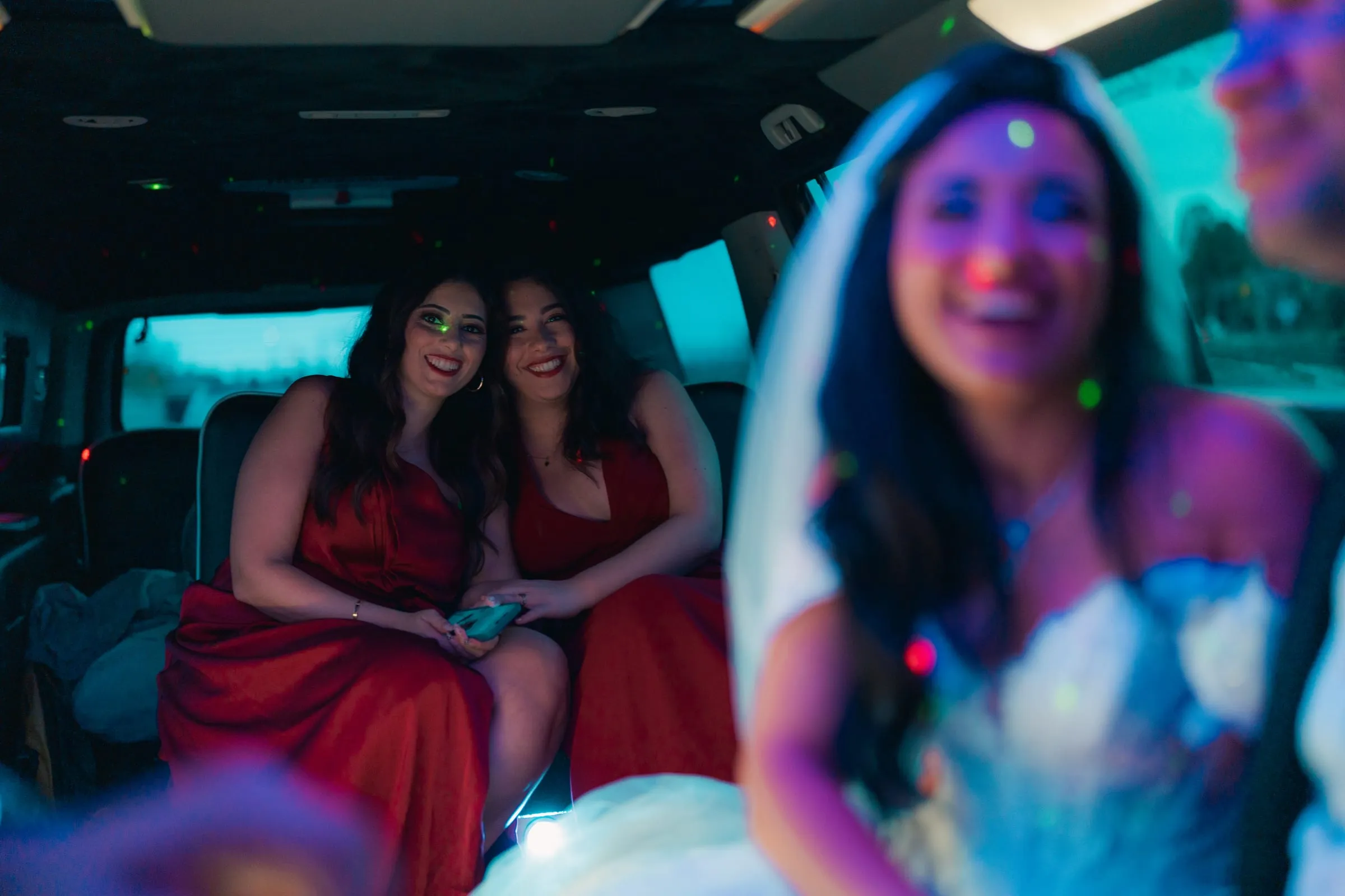 Mariam laughing in the limo as two bridesmaids in red smile behind her