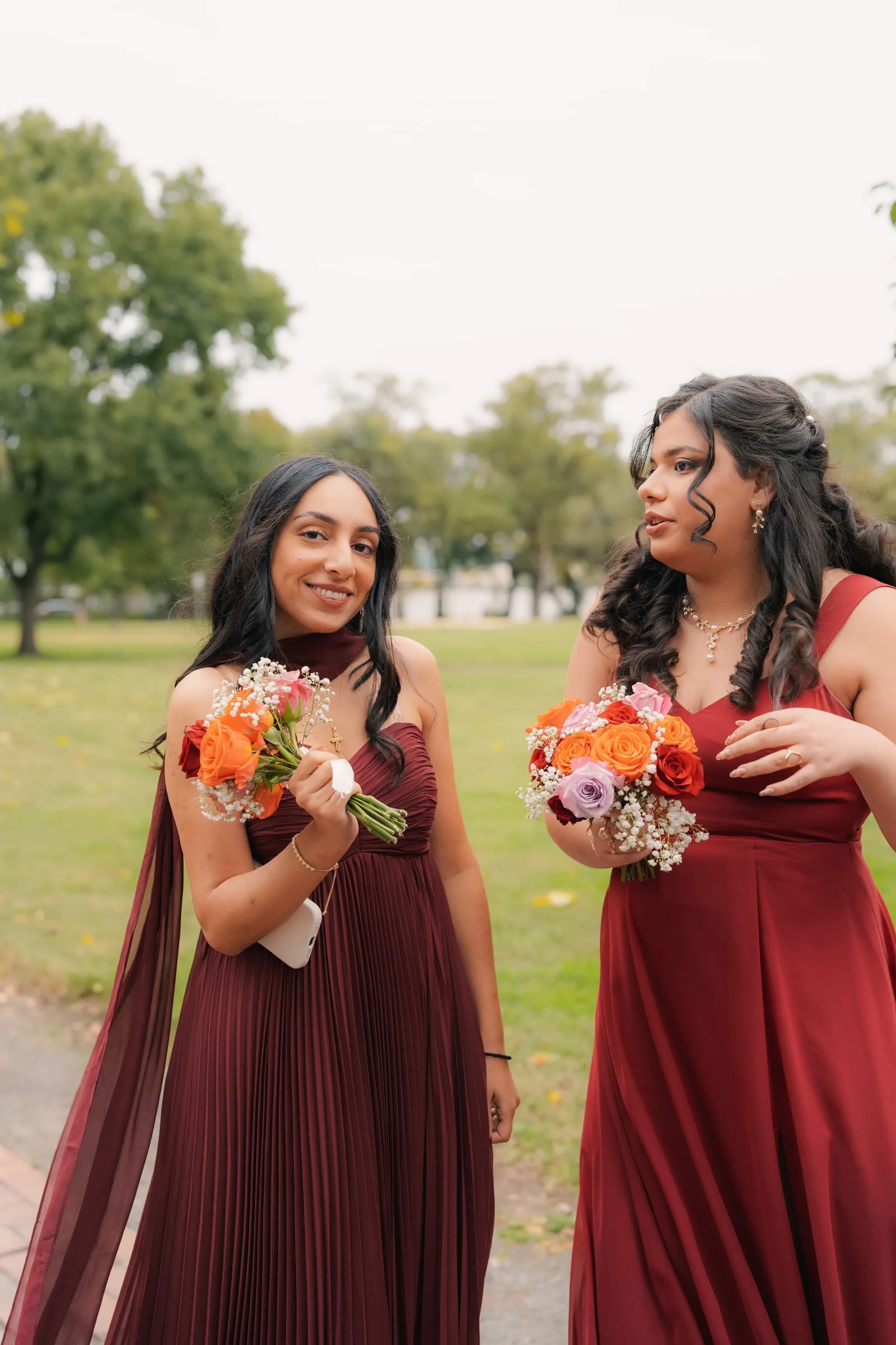 Two bridesmaids in wine red dresses holding bouquets in the park before the wedding