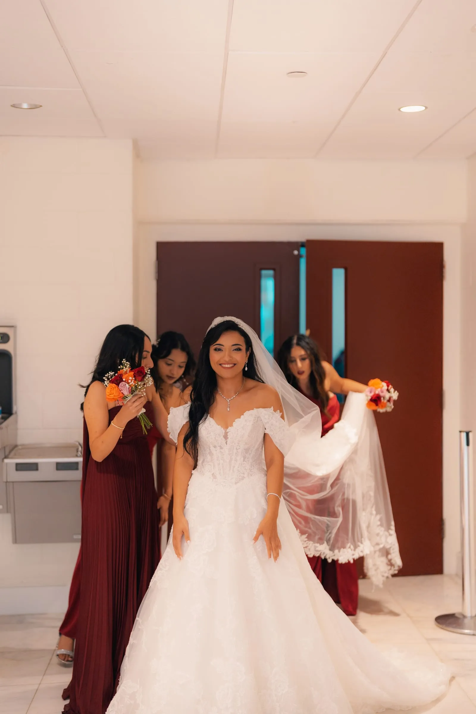Mariam smiling as her bridesmaids arrange her veil before walking into the church