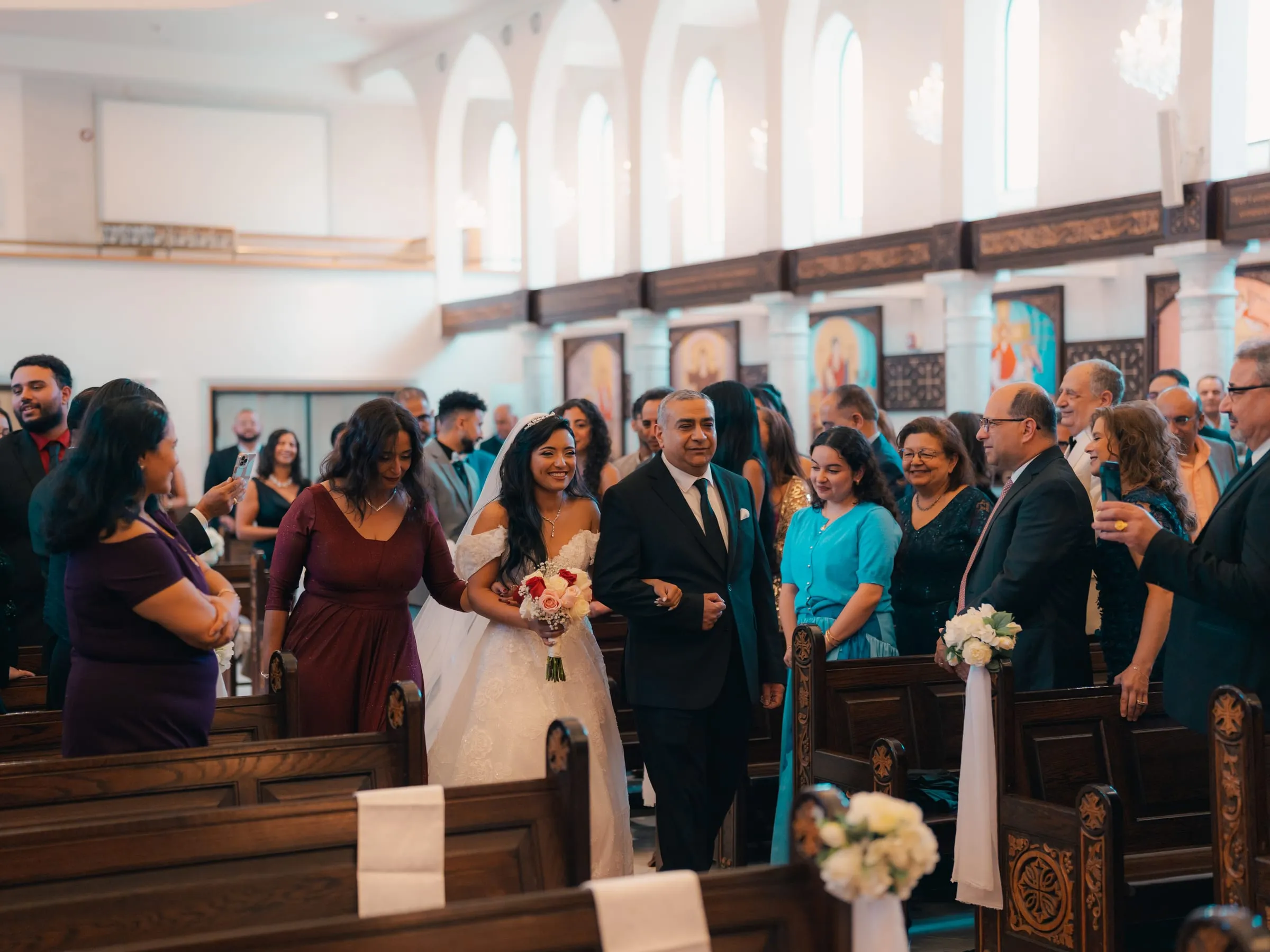 Mariam walking down the aisle with her parents as guests look on