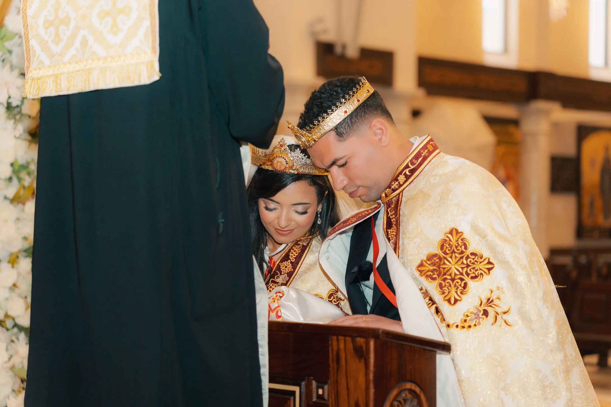 Mariam and Mina, crowned, bowing their heads together at the lectern during the service