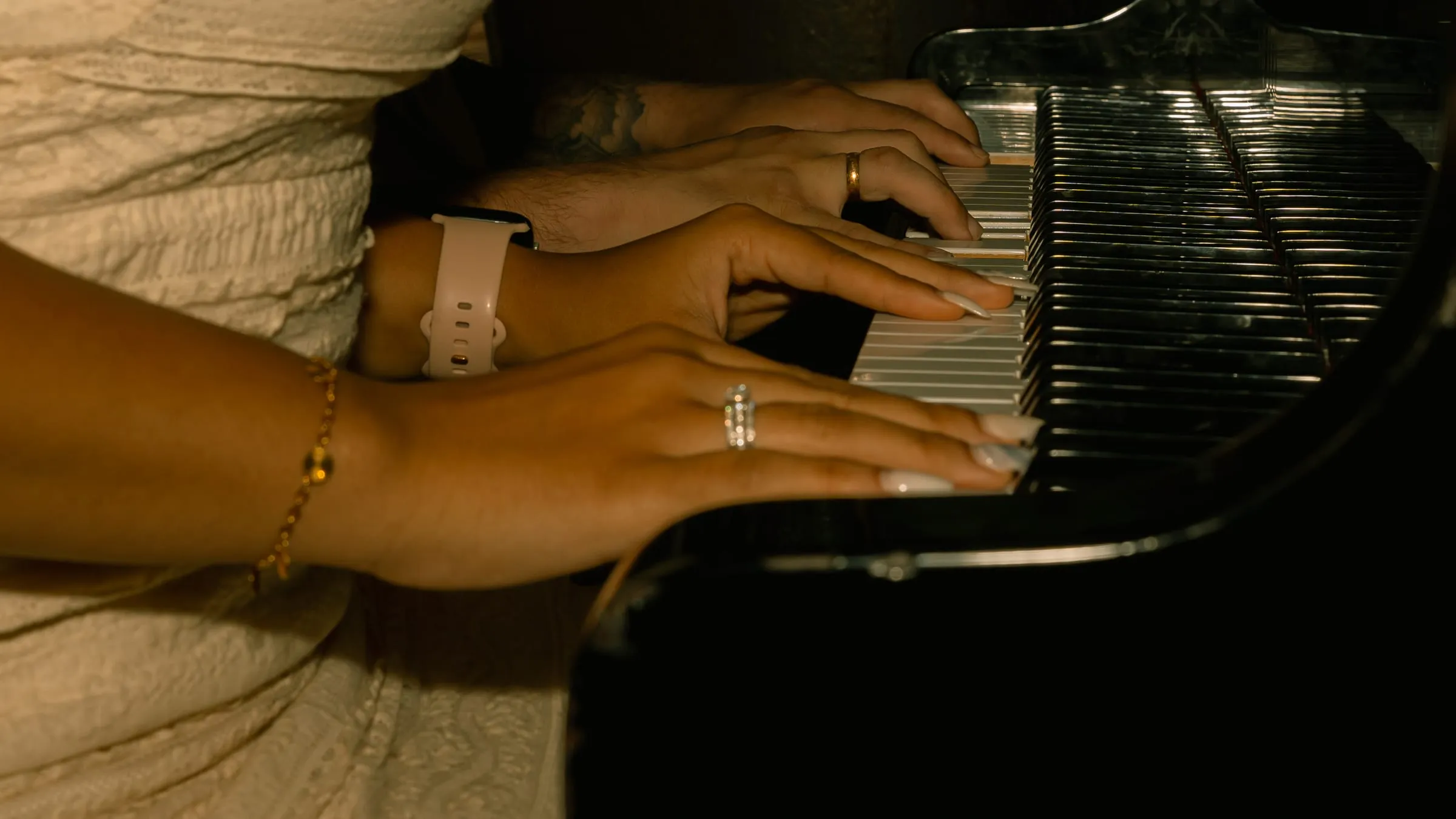 Close-up of Mariam and Thomas's hands resting on piano keys, engagement ring catching the light