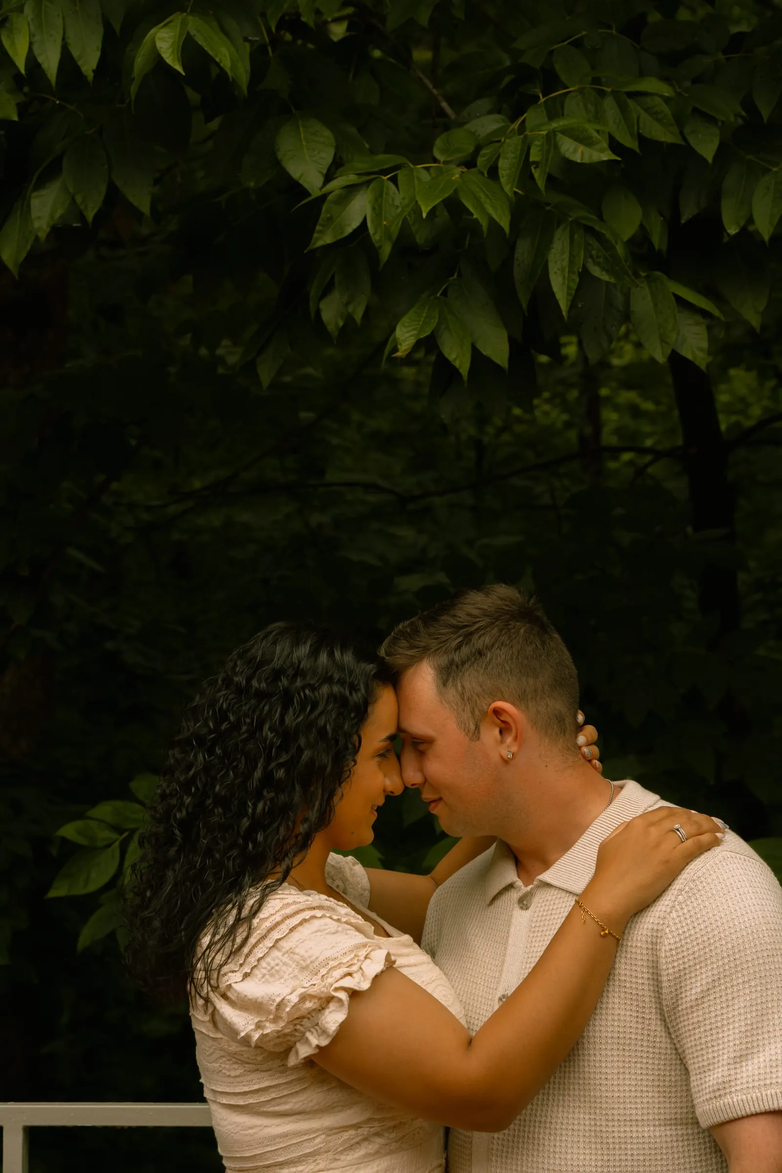 Mariam and Thomas resting their foreheads together beneath the trees