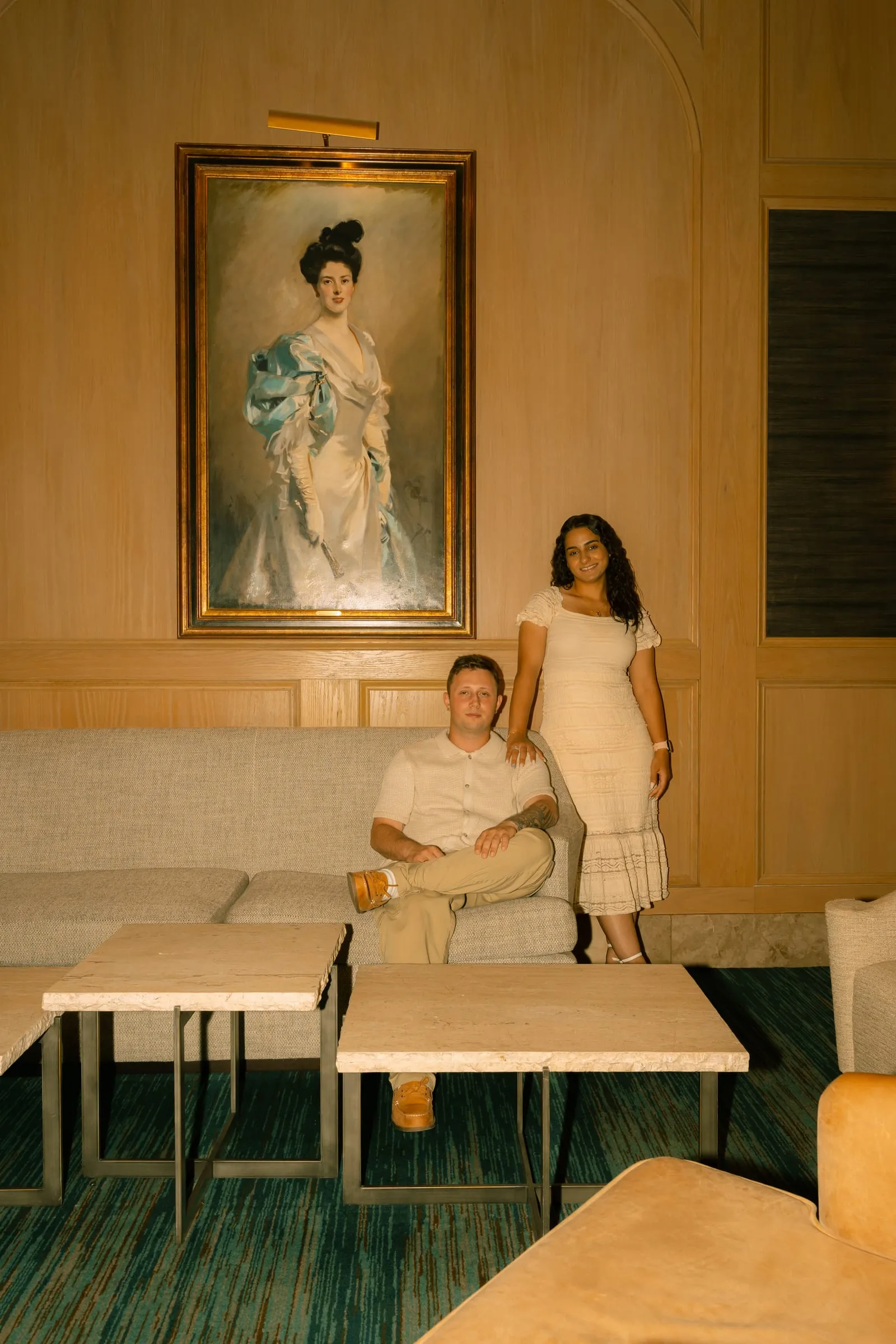 Mariam and Thomas posing beneath a vintage oil painting in the hotel lounge