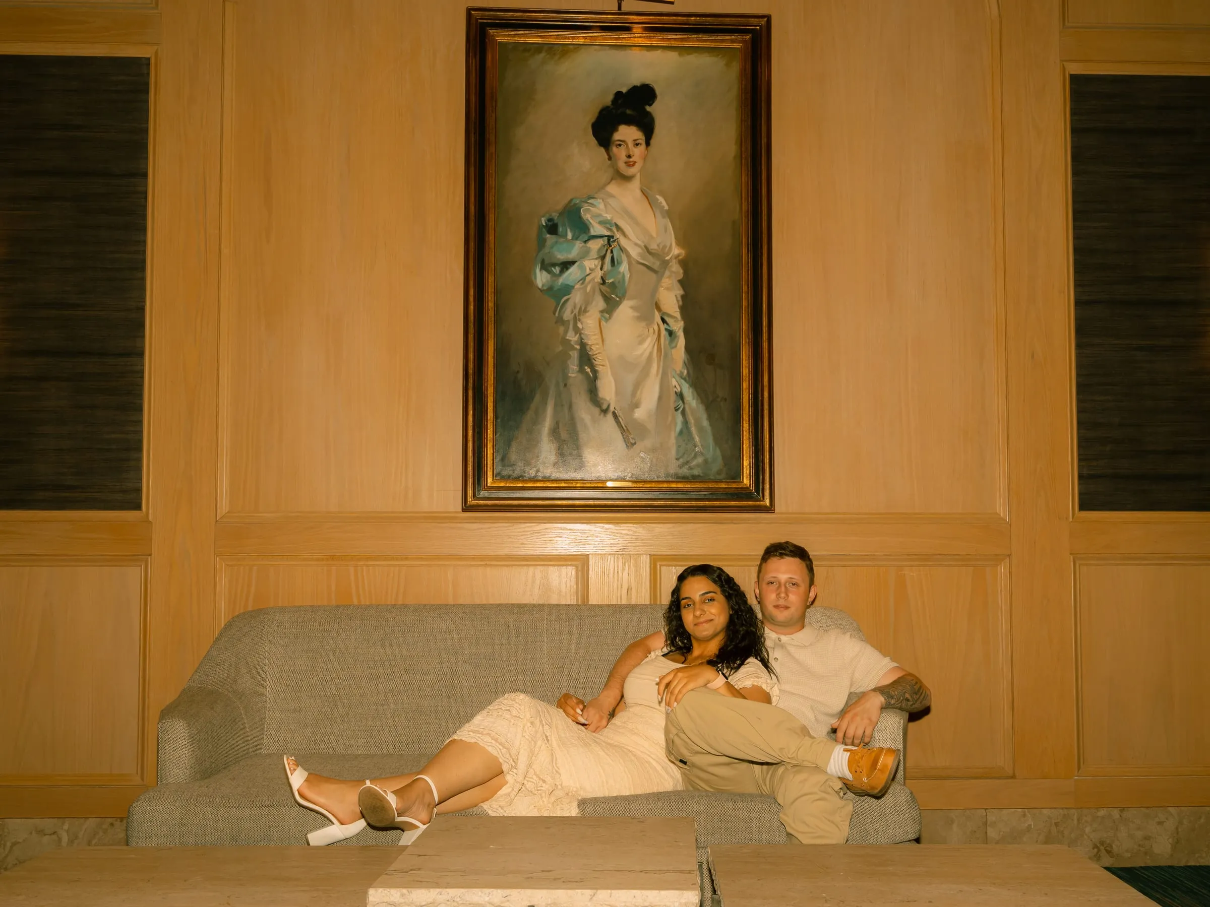 Mariam and Thomas relaxing together on a lounge sofa beneath the painting