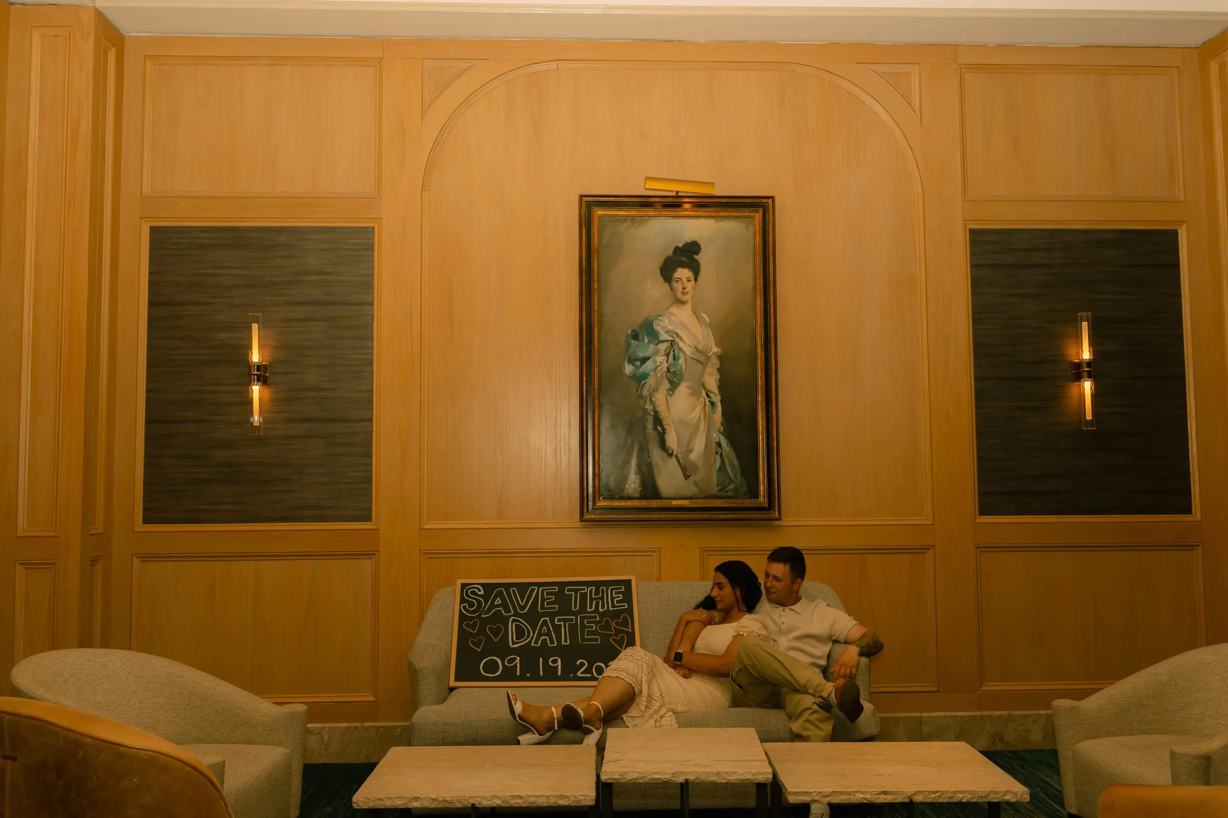 Mariam and Thomas on the sofa beside their Save the Date chalkboard sign