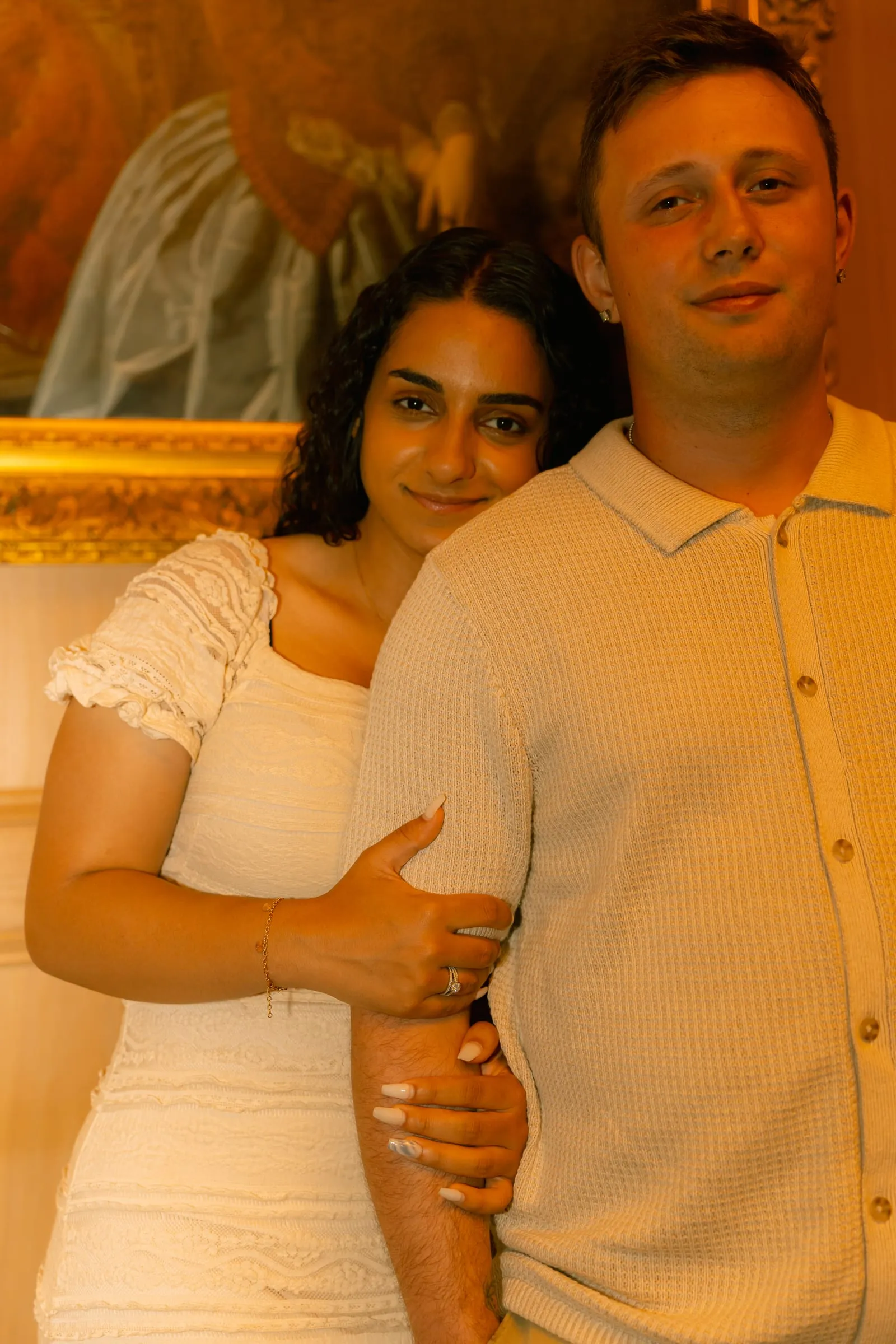Mariam and Thomas standing together in front of a vintage gold-framed painting