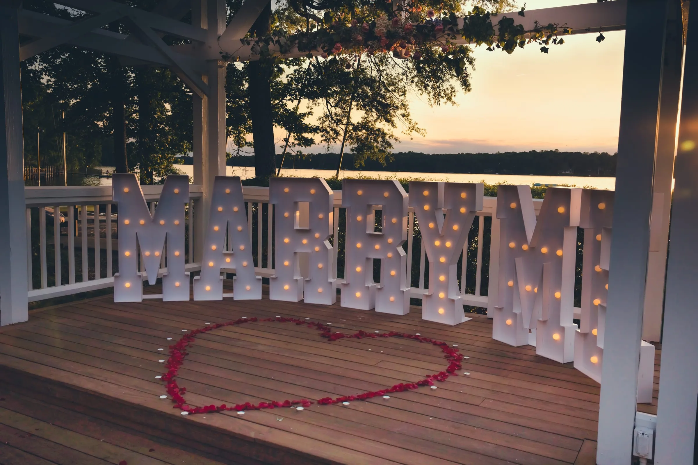 Lit MARRY ME marquee letters and a heart of red rose petals at the Boathouse at Sunday Park